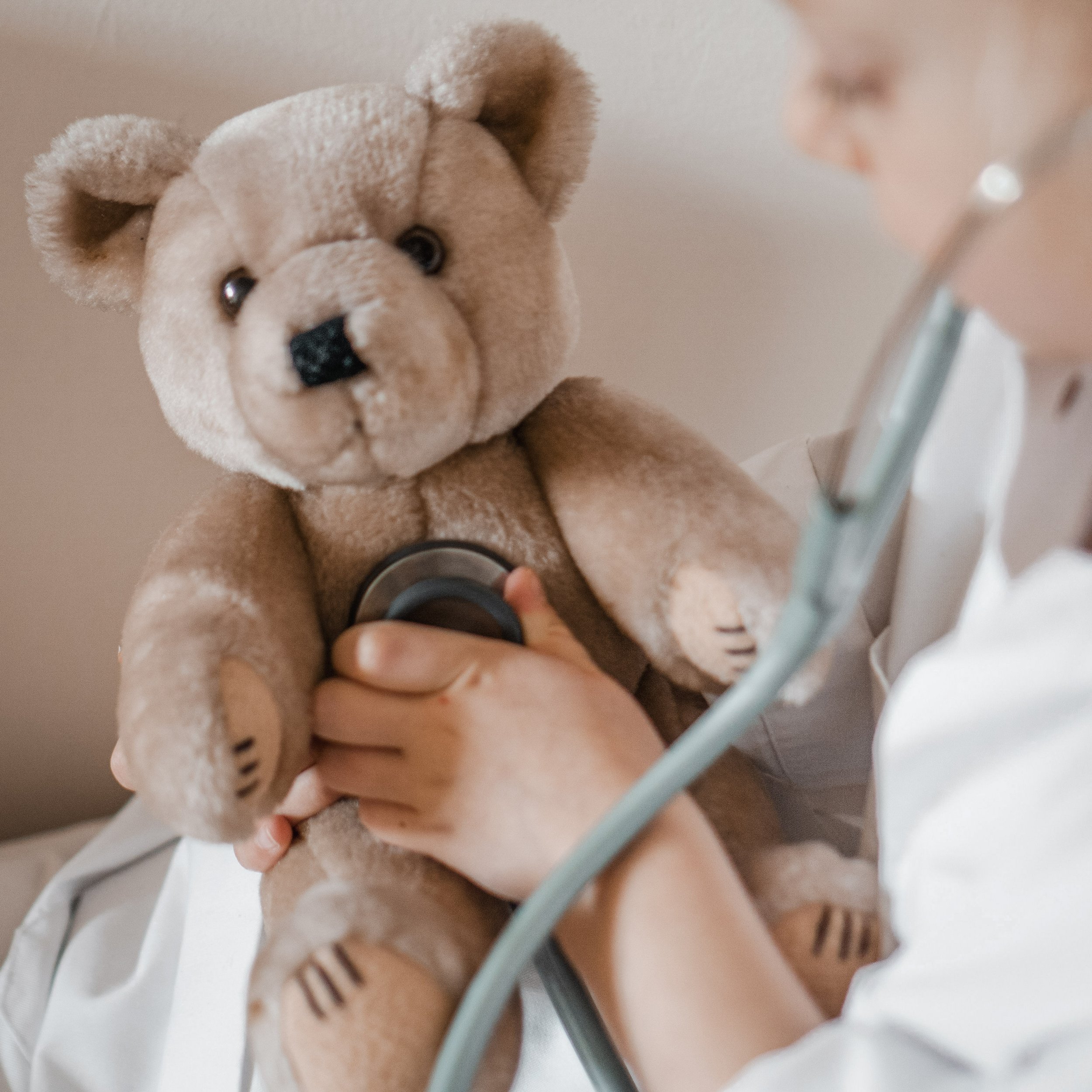 A person in a white coat holding a teddy bear with a stethoscope on its chest.