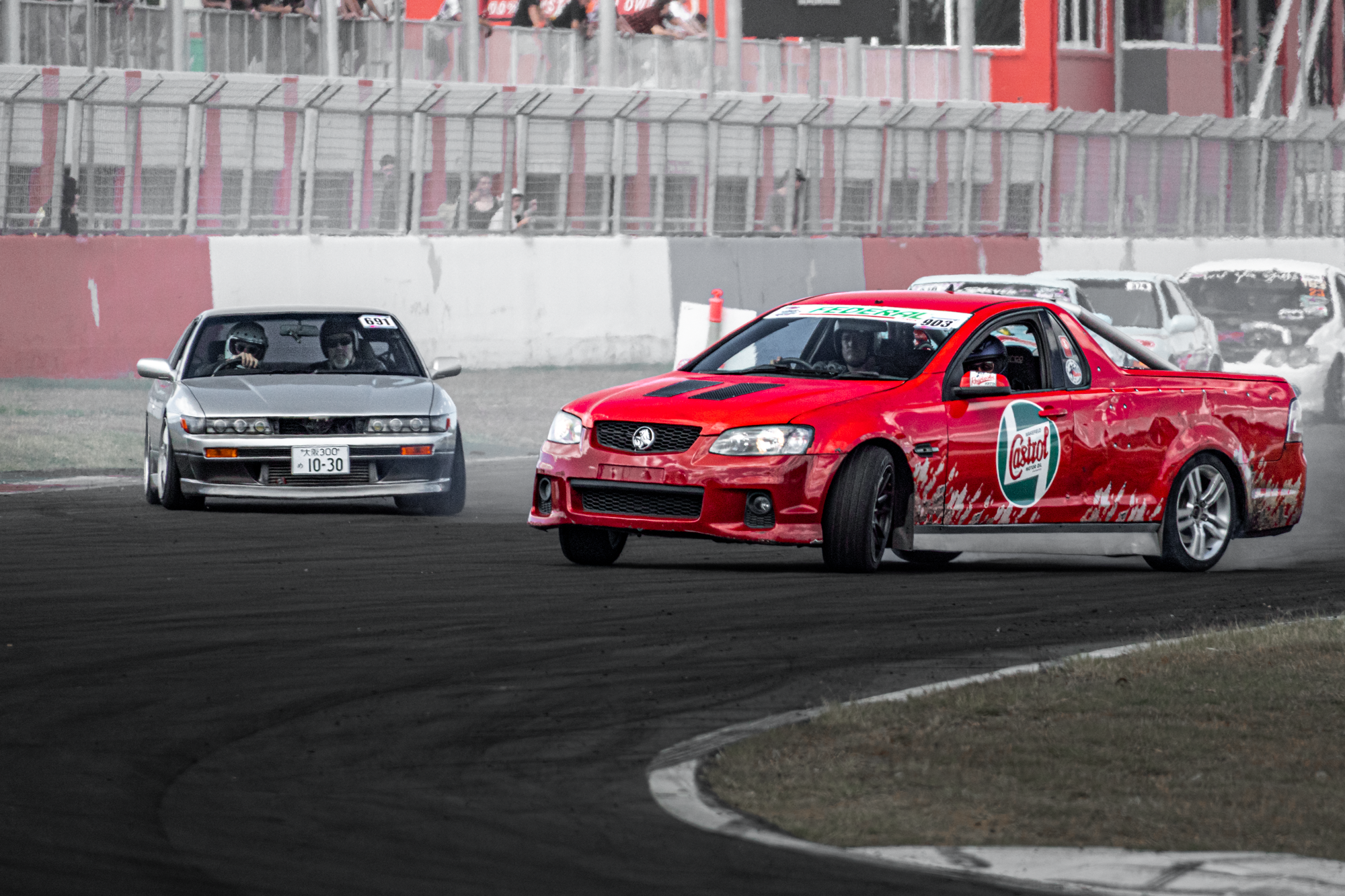 Race cars on a dirt track during a race, with spectators watching from the stands.