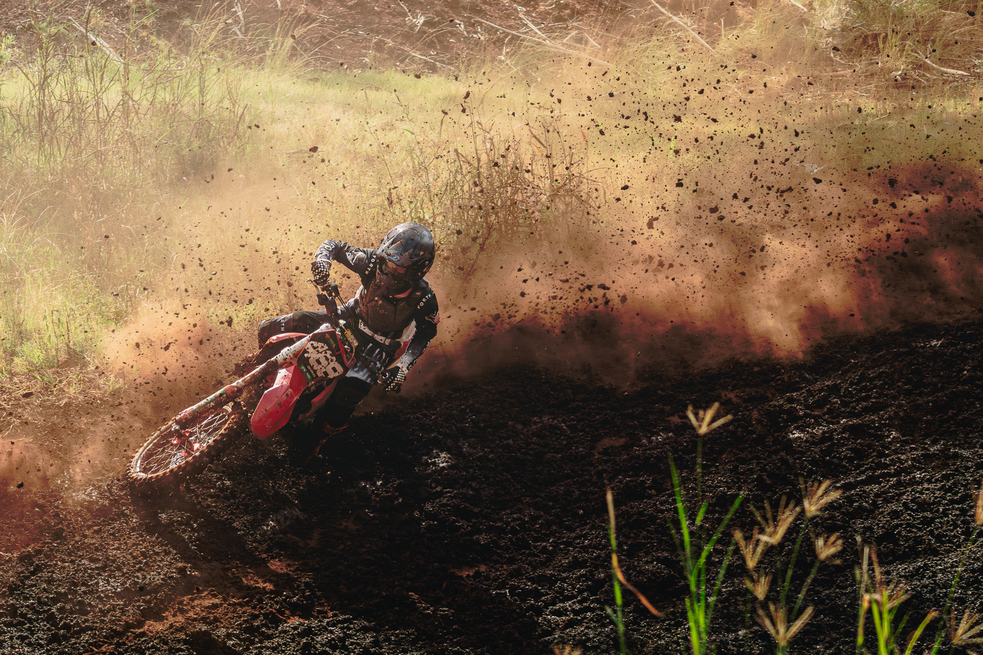A motocross rider in gear and helmet navigating a dirt track, kicking up a large cloud of dirt and debris.