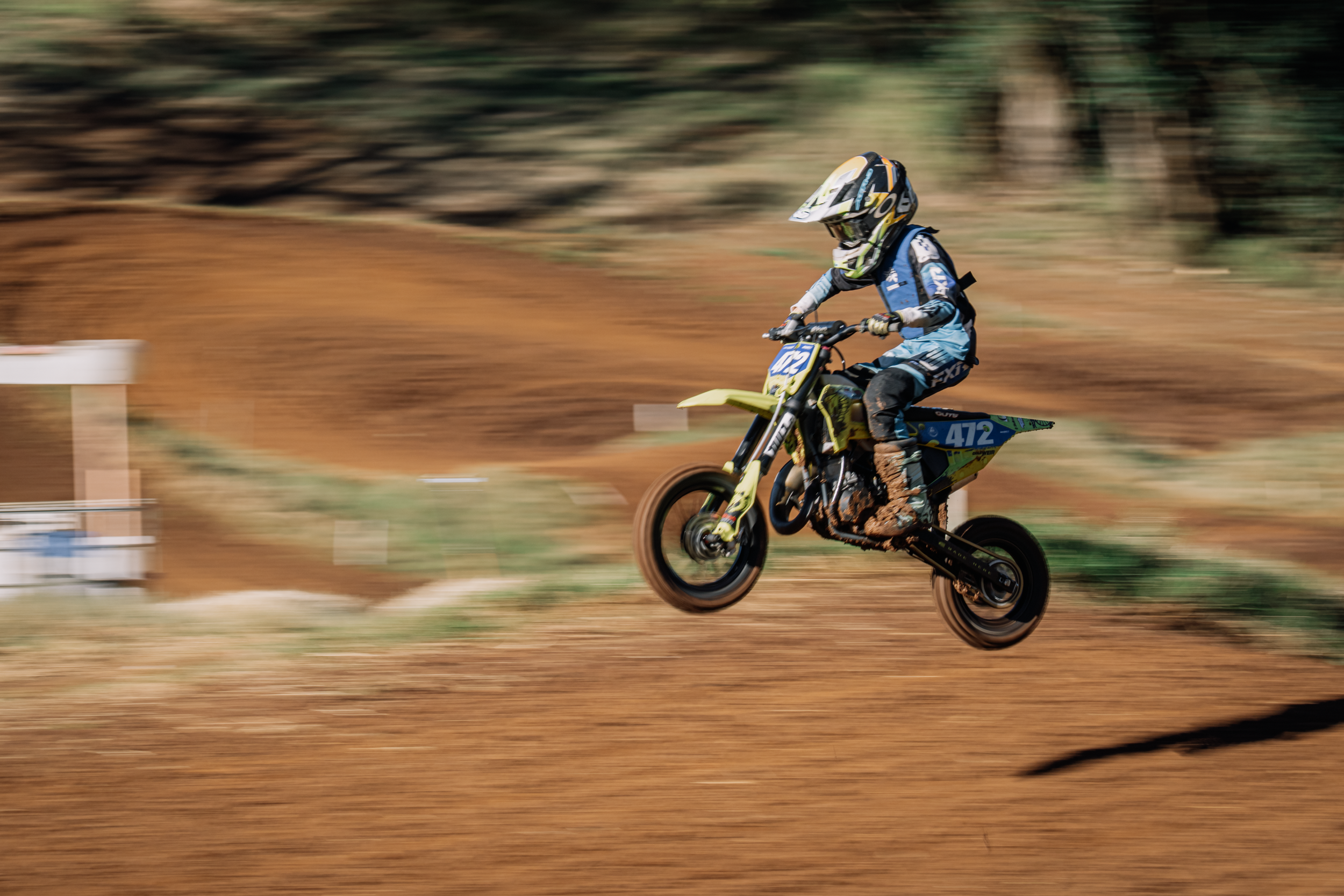 A motocross rider in mid-air on a dirt track with a blurred background showing motion and speed.