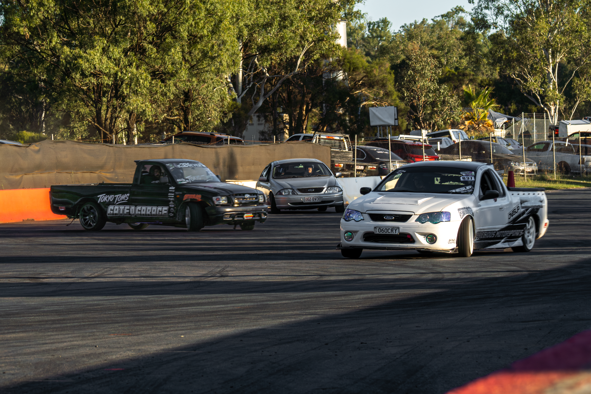 Race cars on a track with a fence and trees in the background, during daytime in a racing event.
