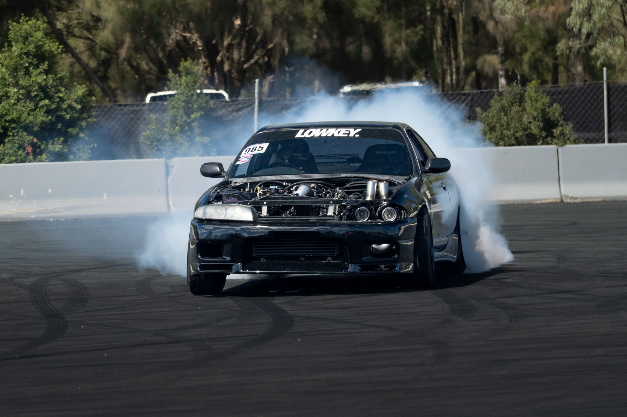 A black sports car performing a burnout on a racetrack, emitting smoke from the tires.