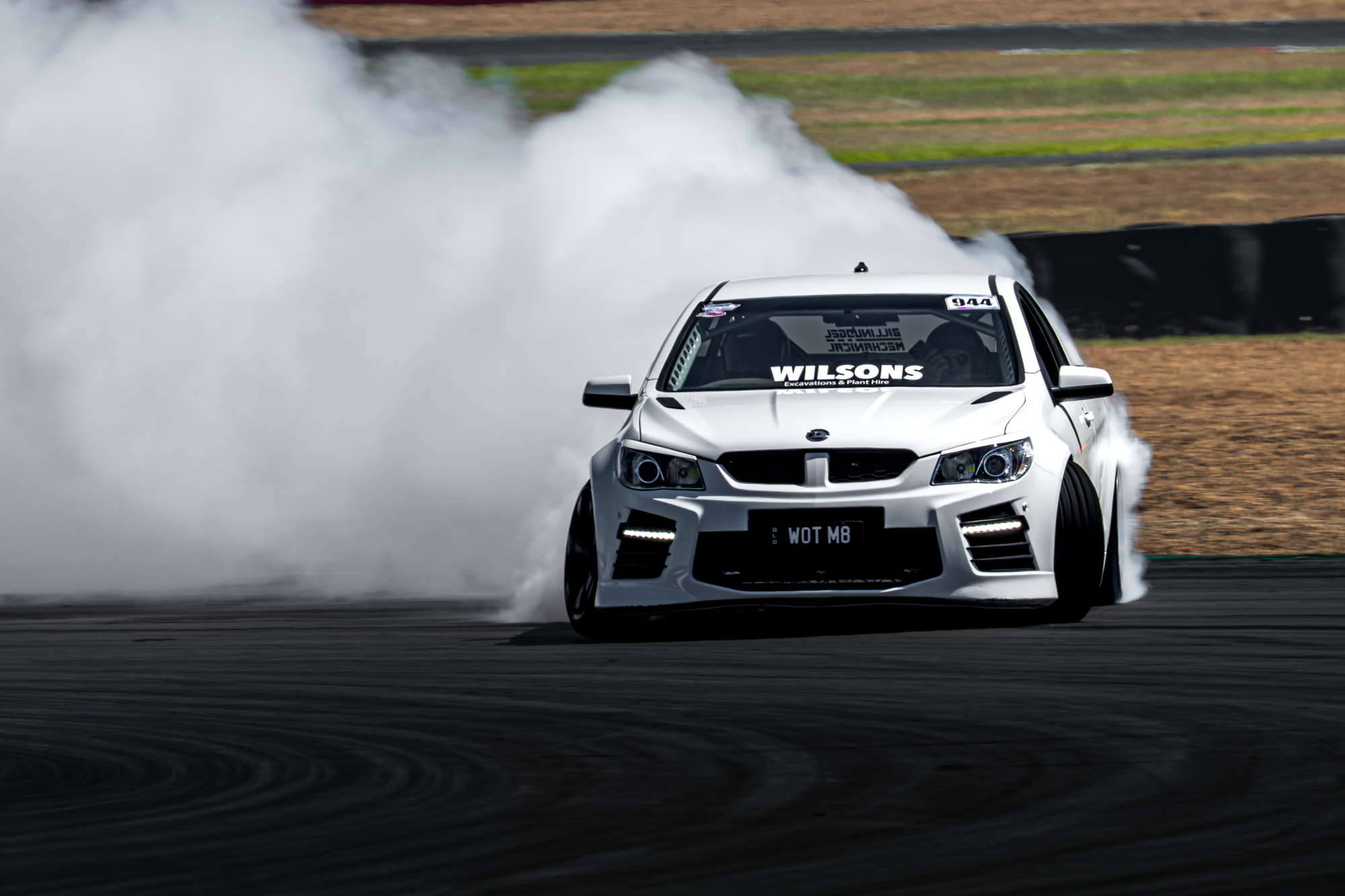 A white race car drifting on a track, creating a large plume of white smoke behind it.