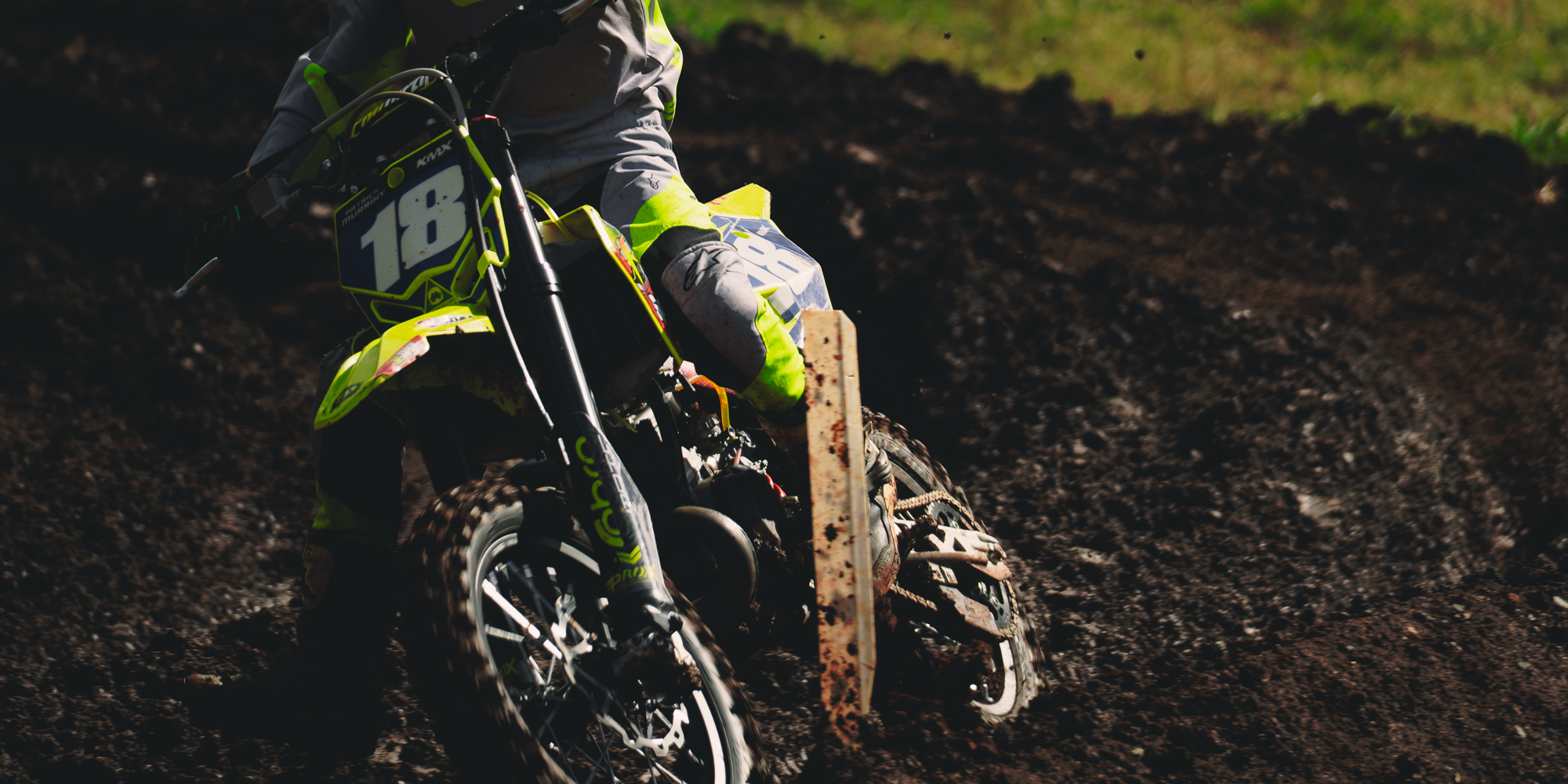 A motocross rider in neon yellow and gray gear riding a dirt bike on a muddy track.
