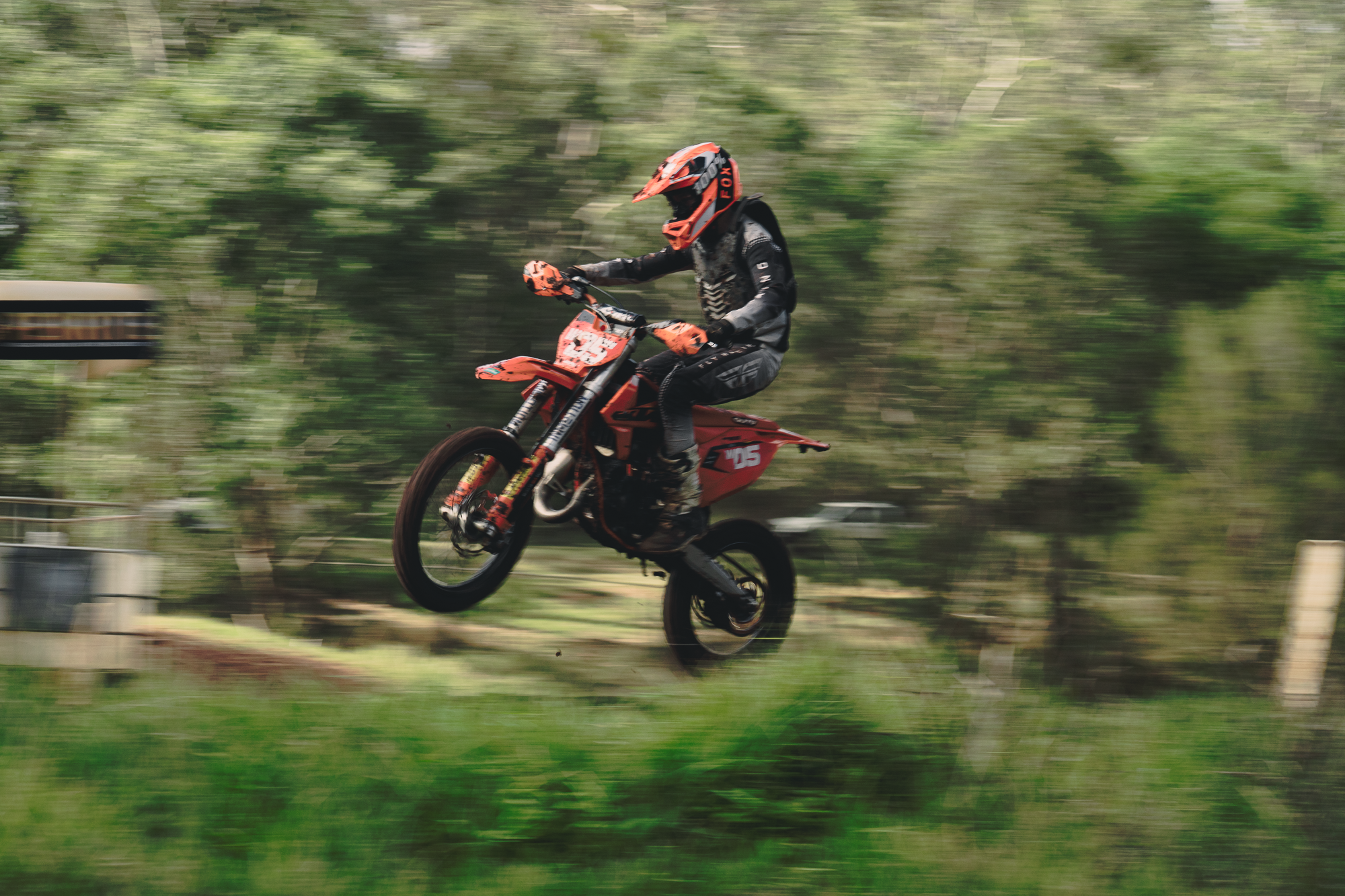 A person wearing a helmet and riding a red dirt bike in a wooded outdoor area.