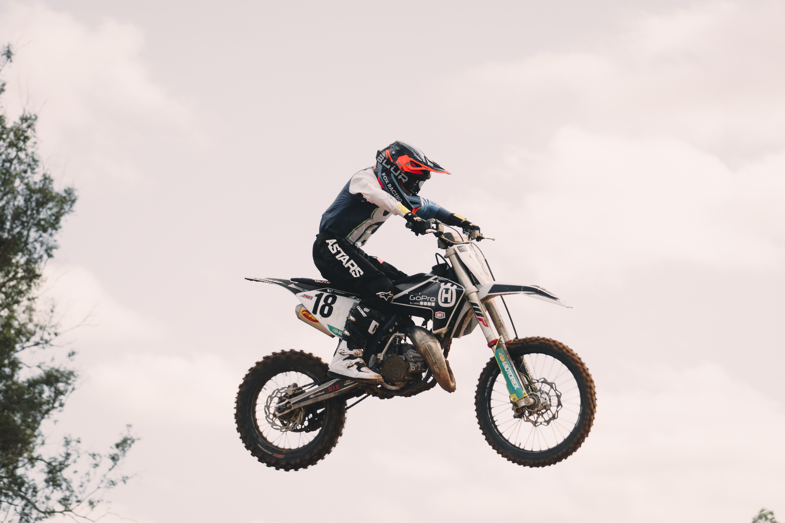 Motocross rider wearing a red and black helmet riding a dirt bike in the air during a jump outdoors.