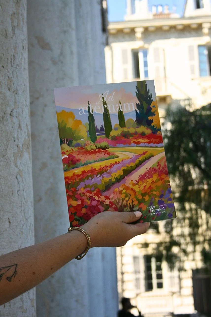 Une main tient le carnet de mariage Ad Æternam, couverture illustrée d'un paysage provençal avec la mention "Pour qu'à jamais l'amour se souvienne"