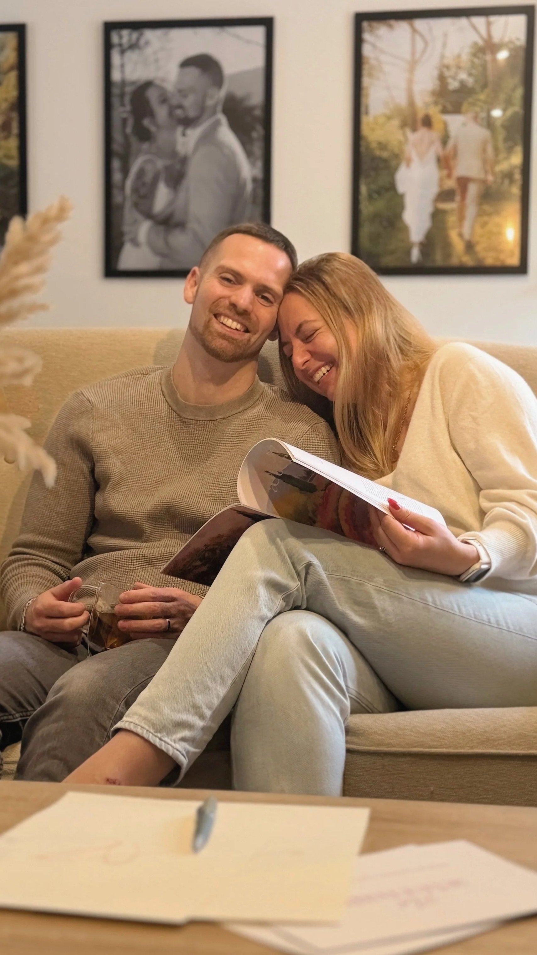 Un couple souriant feuilletant son carnet de mariage et journal de souvenirs Ad æternam sur un canapé.