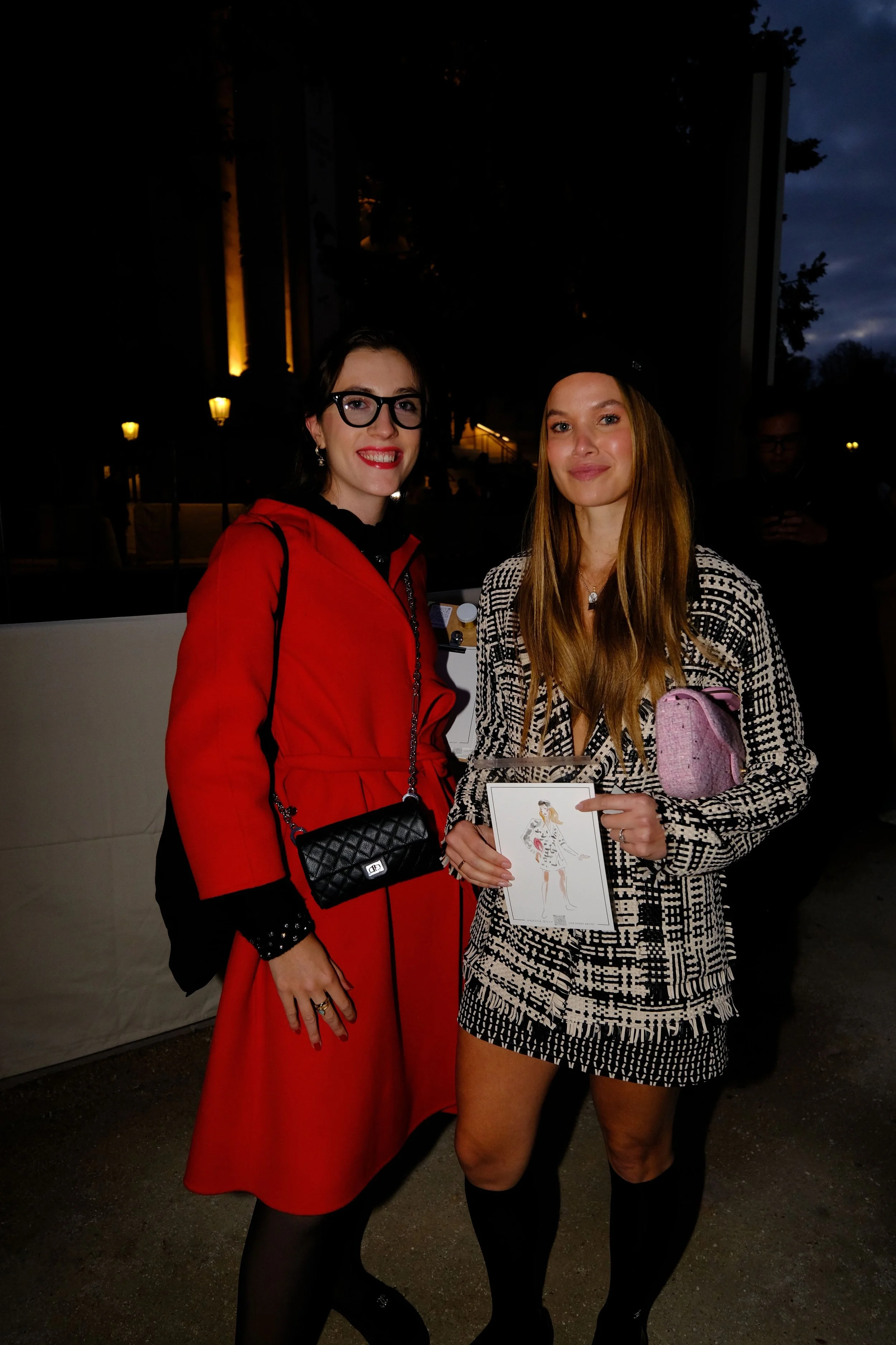 Deux femmes posent ensemble, une portant une robe rouge et une autre en tenue à motif noir et blanc, lors d'un événement en soirée.