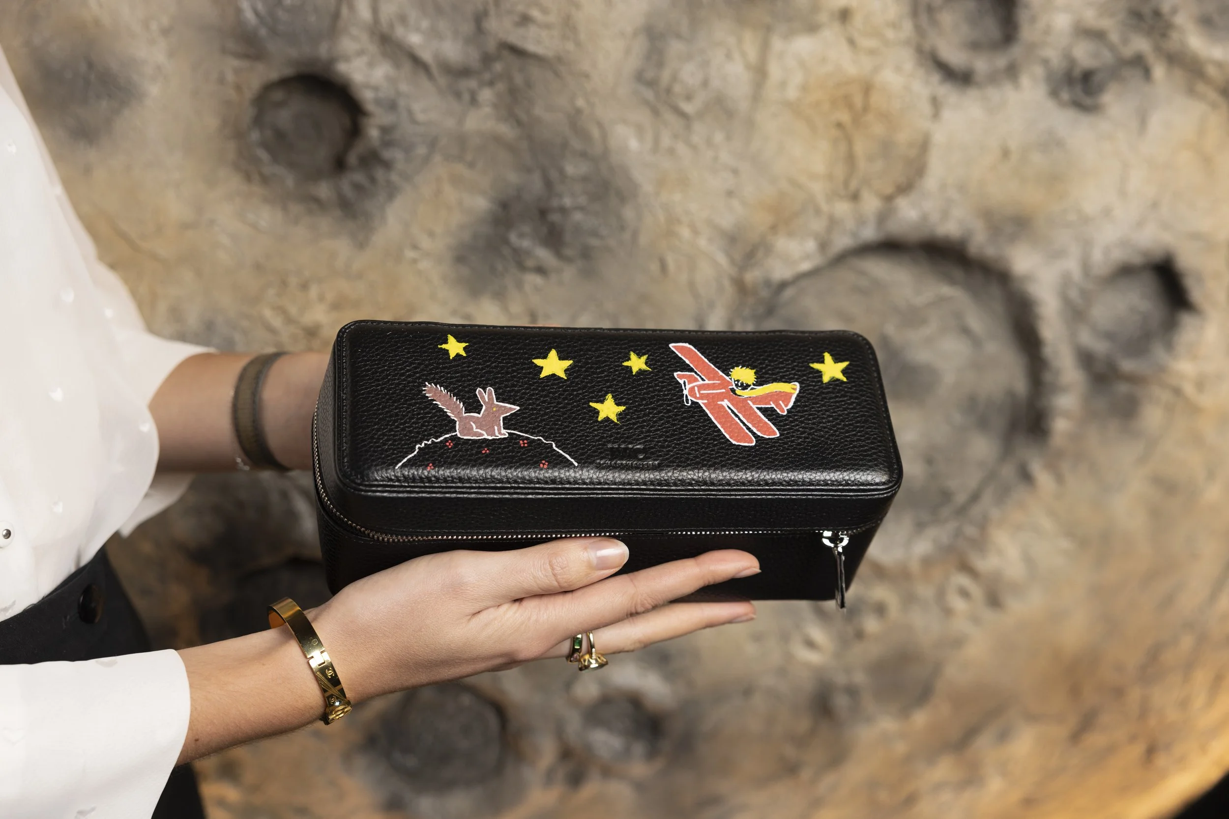 Une personne tient un sac à main noir avec des broderies d'un lapin et d'un avion, entourés d'étoiles jaunes.