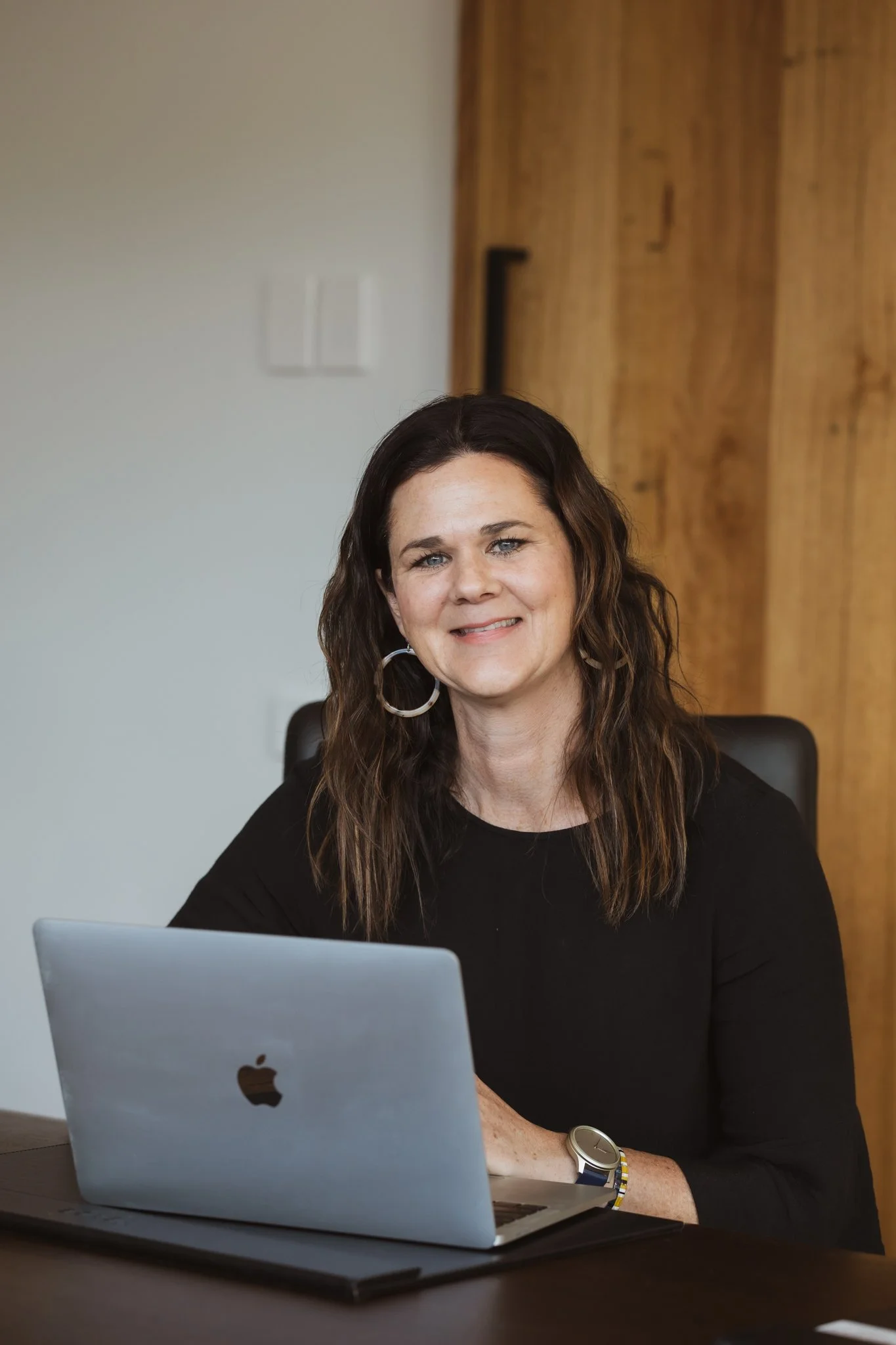 Author and content creator Penny Terry sitting at a desk with a silver MacBook in front of her, smiling, ready to write her blog The Penny Drop.
