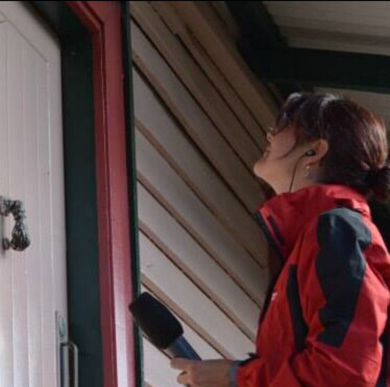 Podcast host Penny Terry knocking on a door, wearing headphones and holding a microphone.