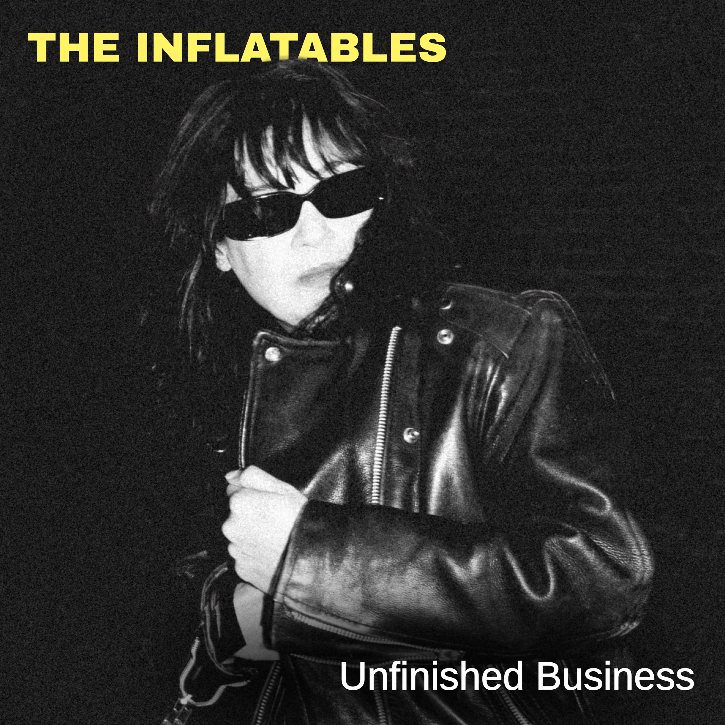 A black and white photo of The Inflatables lead singer, Violetta, wearing sunglasses and a leather jacket, with text 'THE INFLATABLES' at the top and 'Unfinished Business' at the bottom.