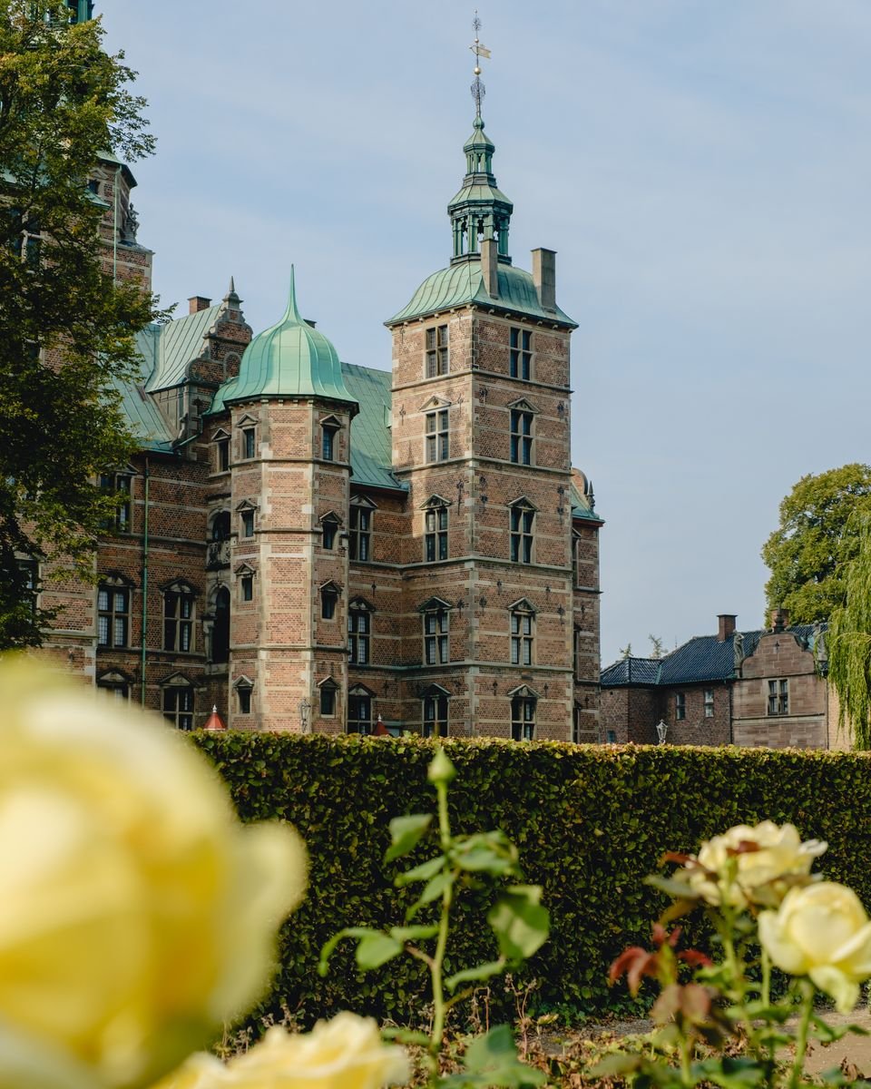 Rosenborg Castle's copper turrets seen through trees, with yellow roses blurred in the foreground