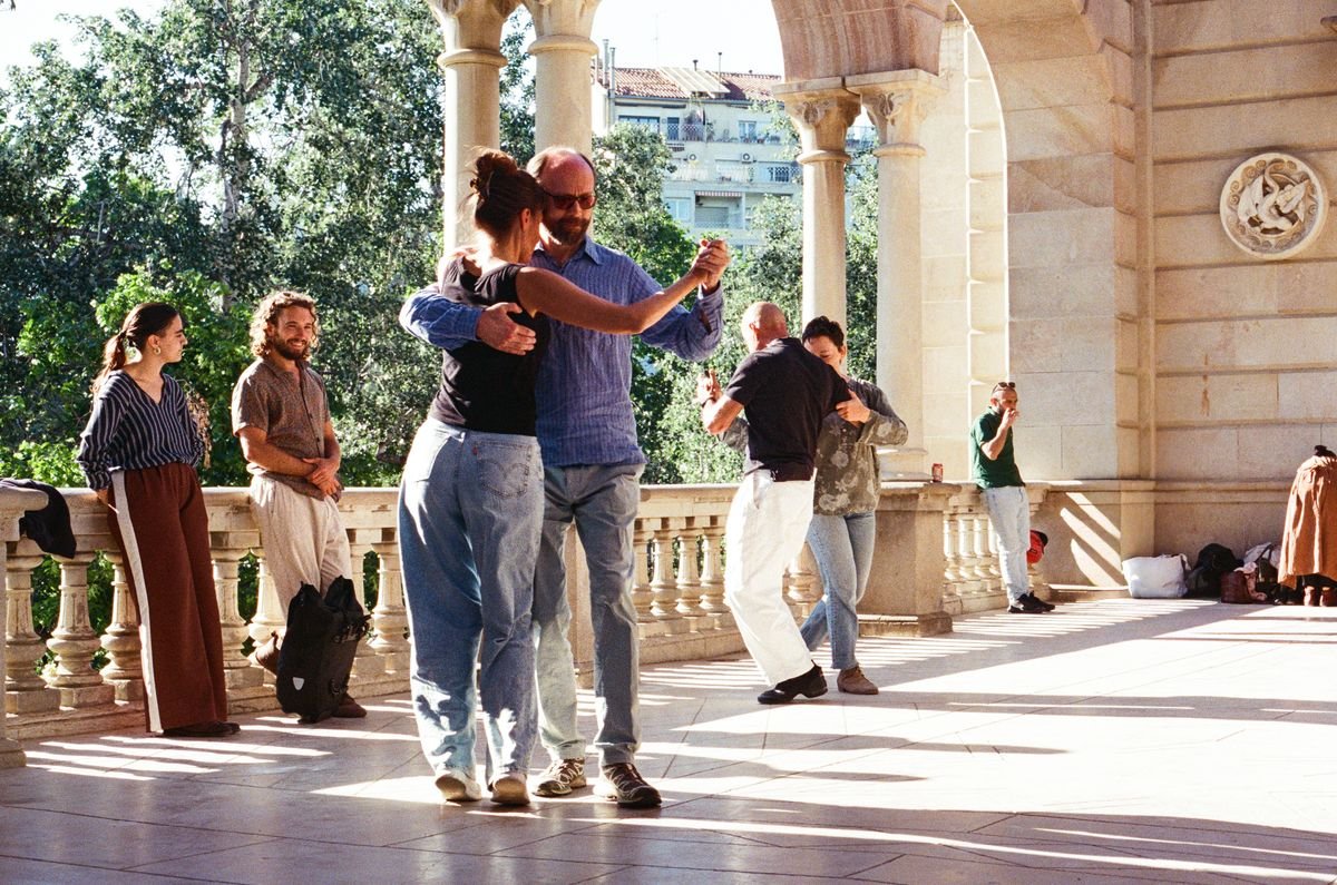 A couple tangos on a colonnaded terrace overlooking the city, other dancers waiting their turn
