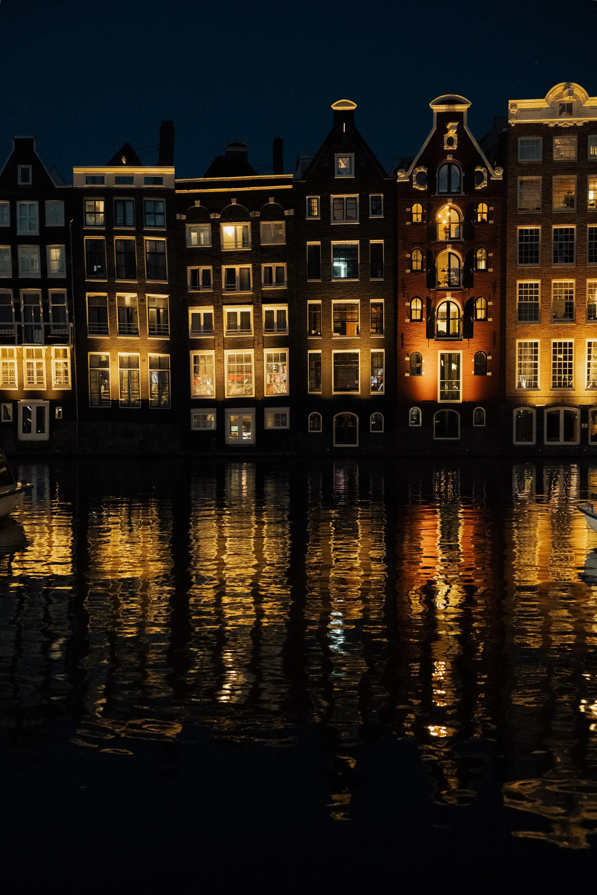 Nighttime view of illuminated buildings along a canal, with reflections on the water.