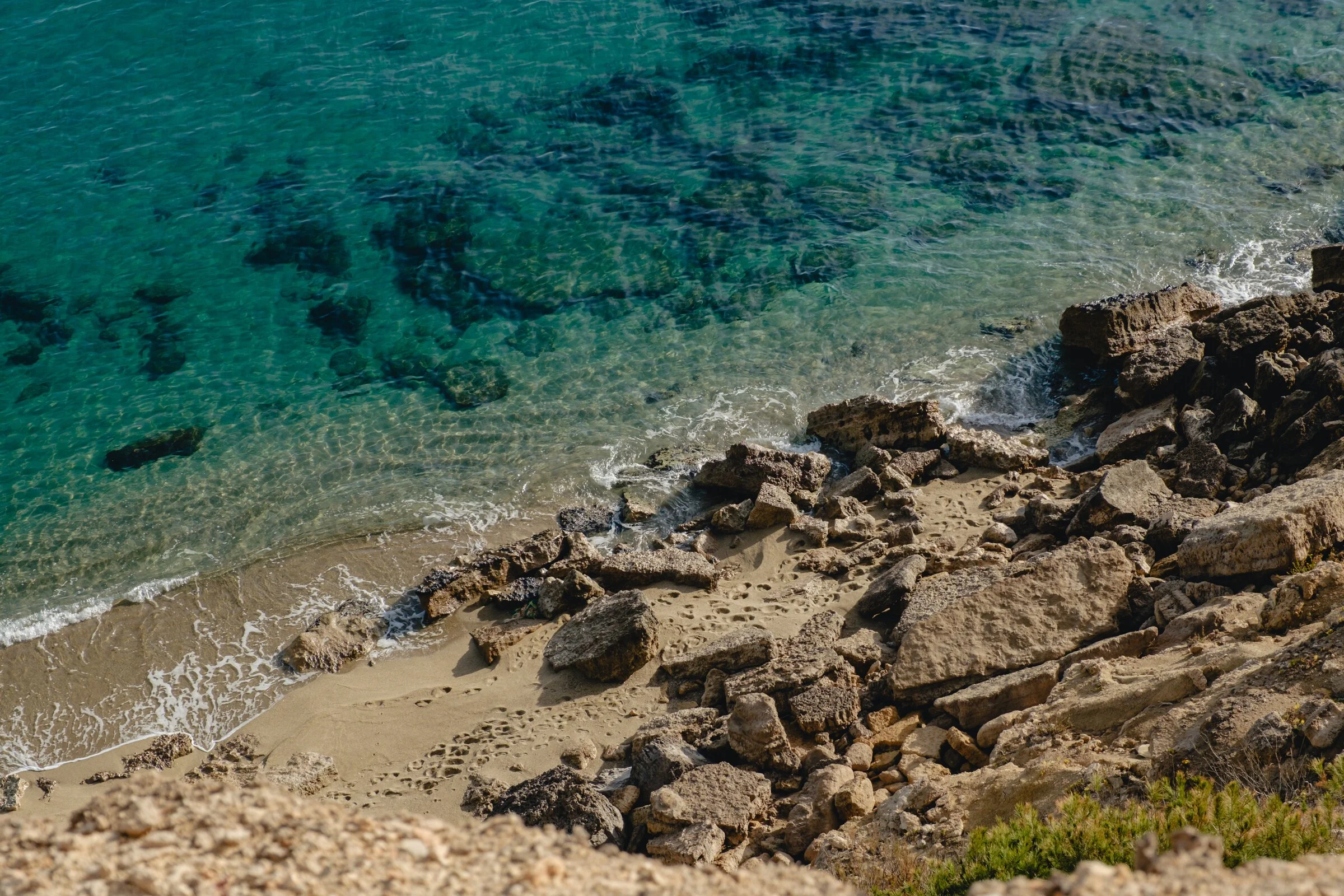 Clear turquoise Mediterranean water laps against a rocky, sun-bleached shoreline on the Cote Vermeille