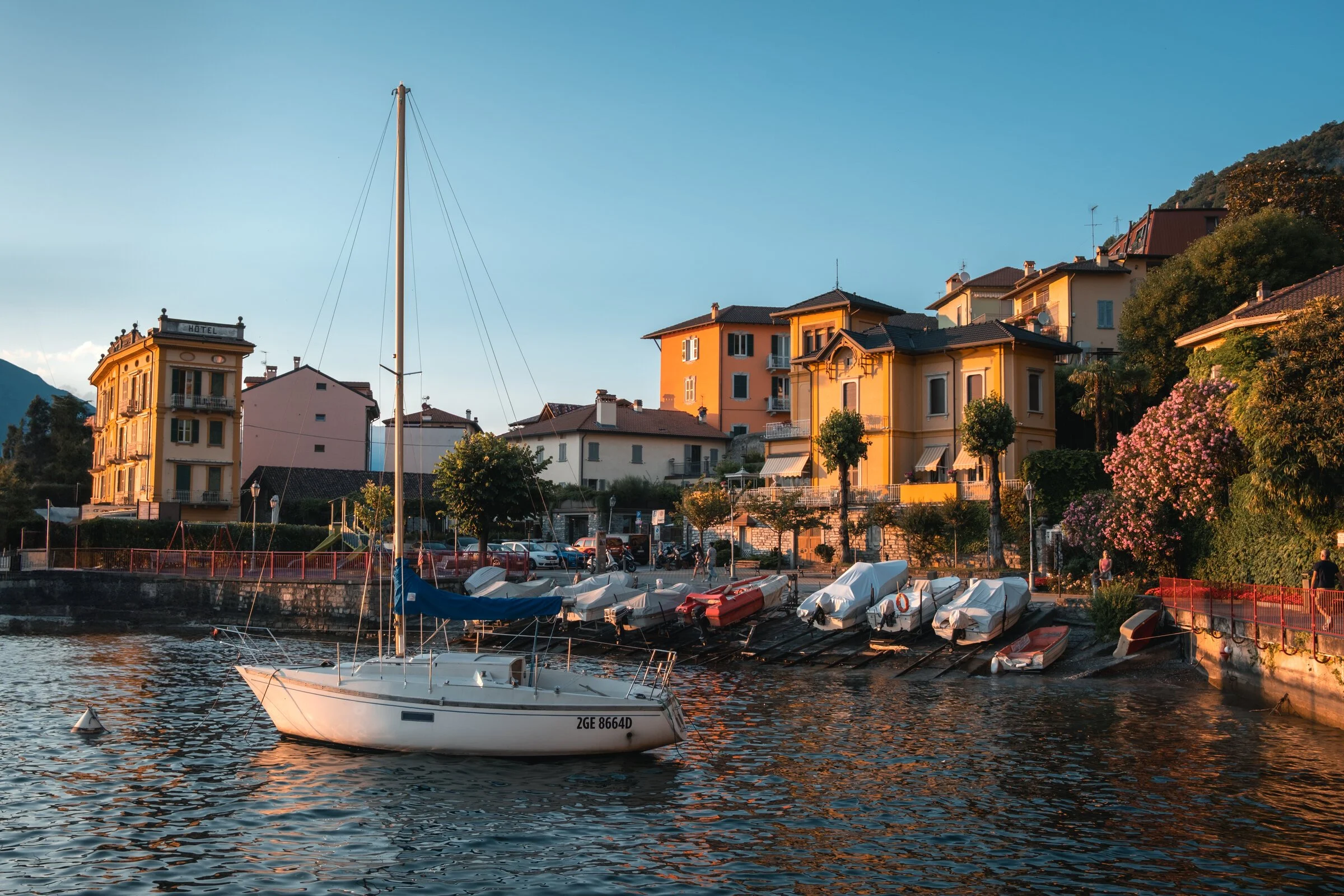 A sailboat rests at anchor before a row of ochre and pink lakefront villas on Lake Como at golden hour