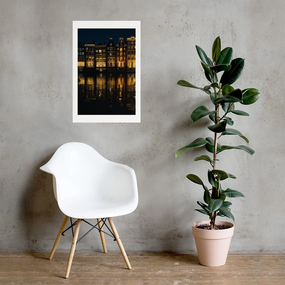Night photograph of Amsterdam canal houses glowing against dark water. Elegant European city wall art print.