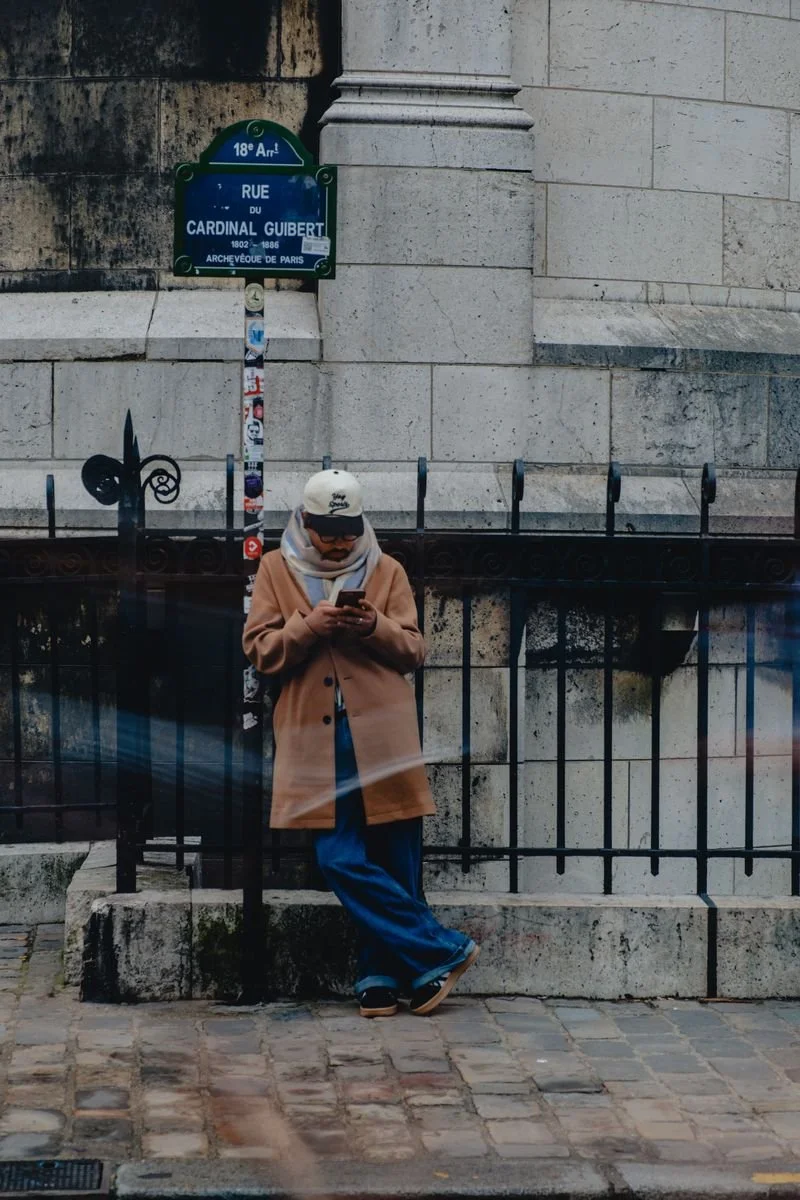 A person checks their phone against the stone wall beneath Sacré-Cœur on Rue du Cardinal Guibert