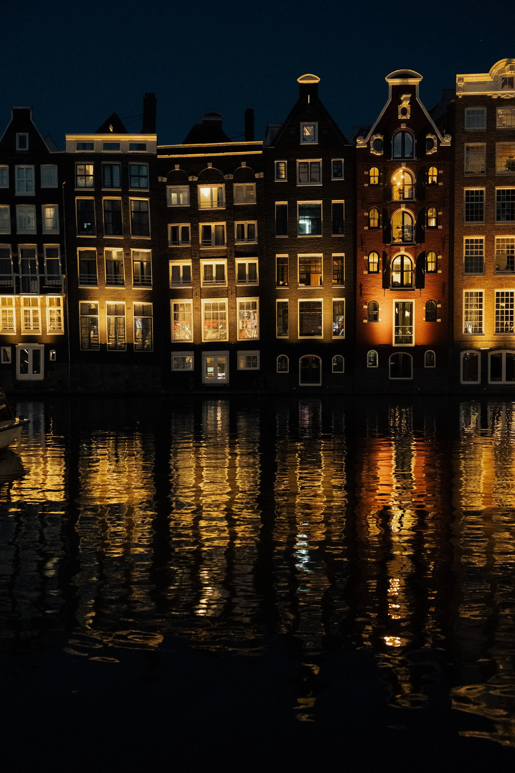 Night photograph of Amsterdam canal houses glowing against dark water. Elegant European city wall art print.