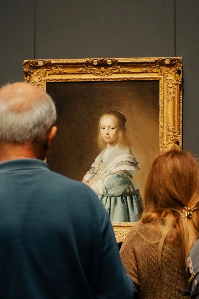 Museum visitors gather quietly before a gilt-framed portrait at the Rijksmuseum