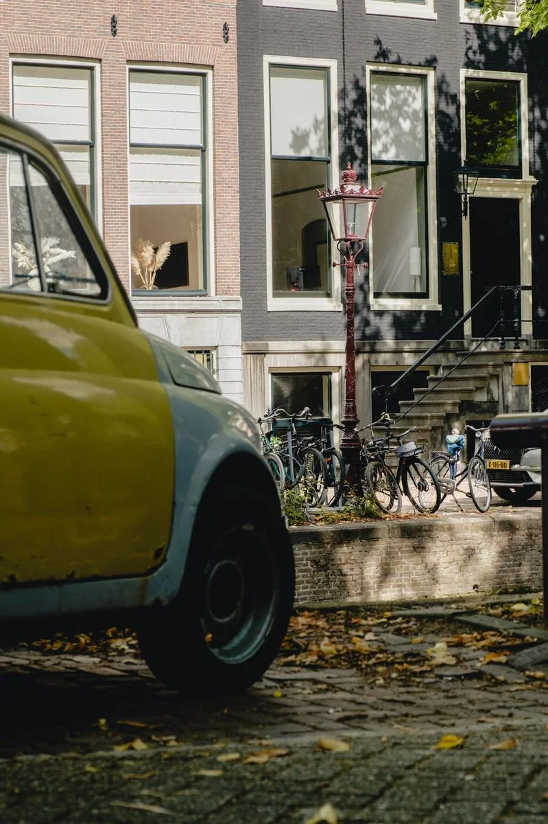 A vintage yellow car parked beneath a lamppost and rows of bicycles
