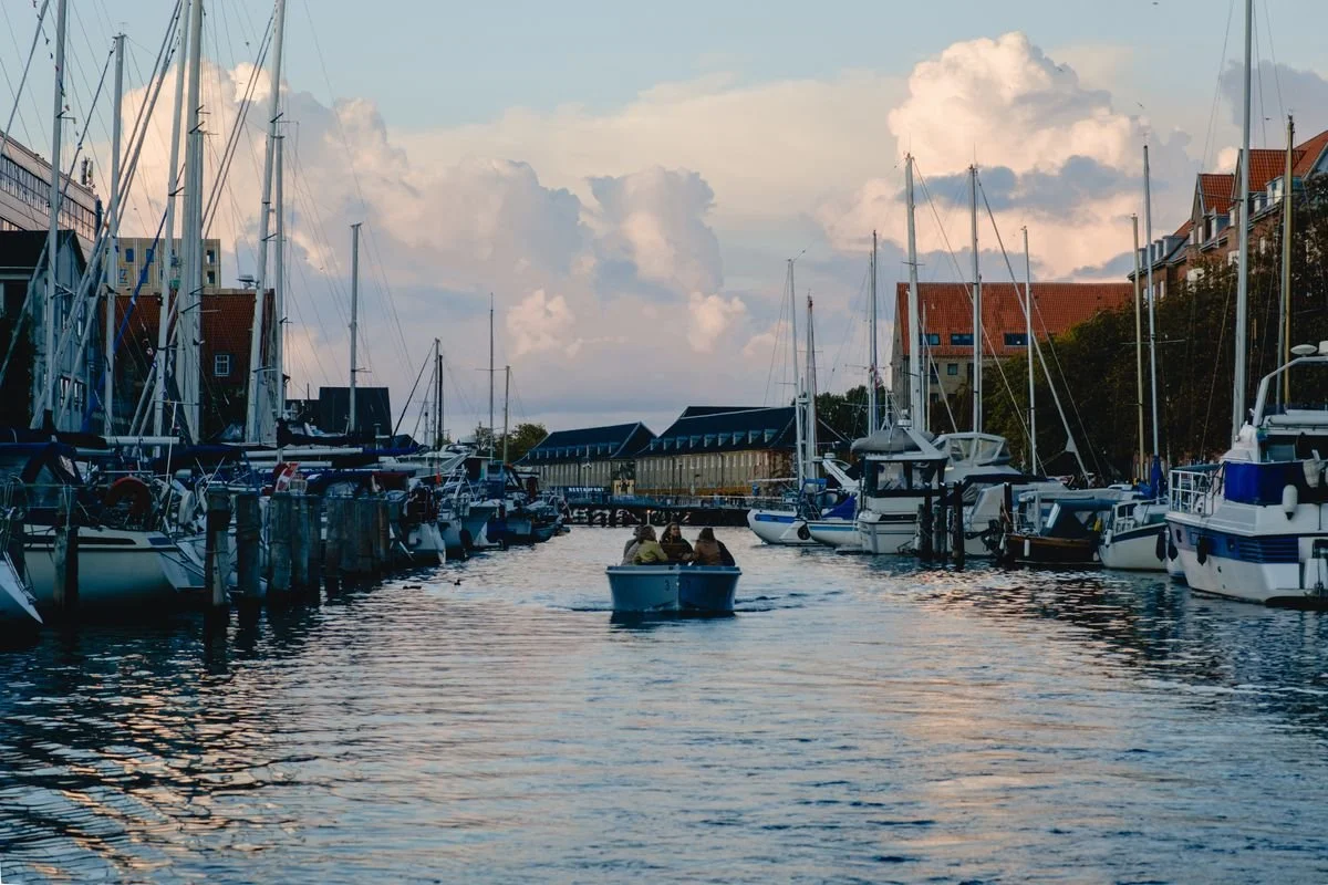 A small passenger boat glides through a marina full of sailboats under a golden evening sky