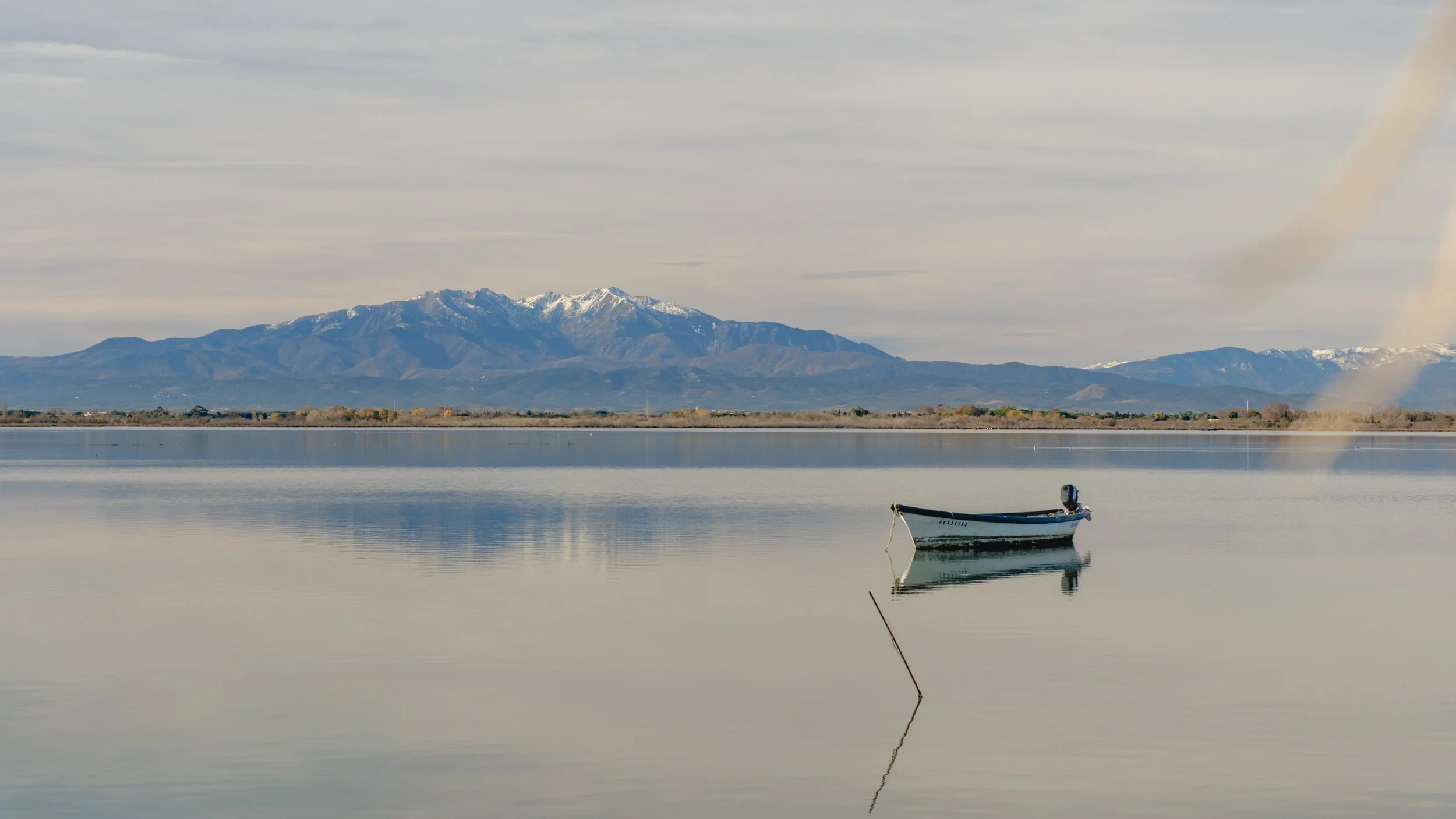 A boat floating on calm water with snow-capped mountains in the background under a cloudy sky.