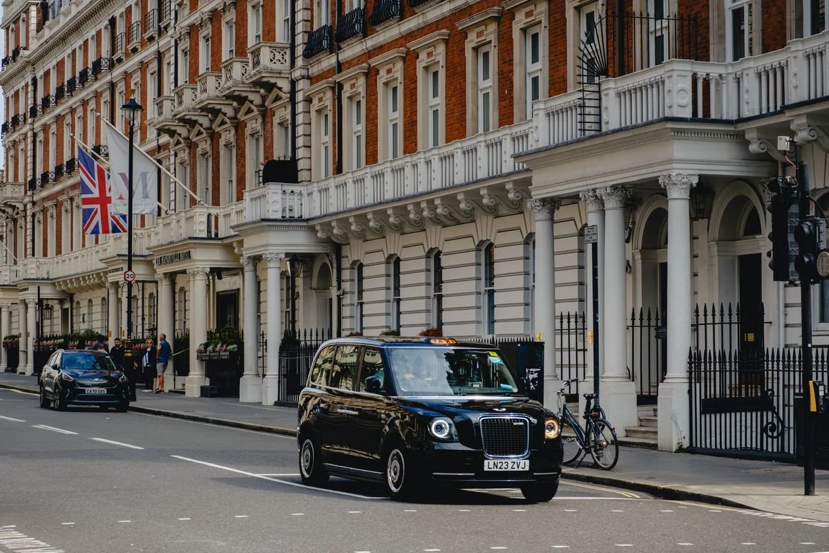 A black taxi rolls past flag-draped red brick townhouses in Mayfair