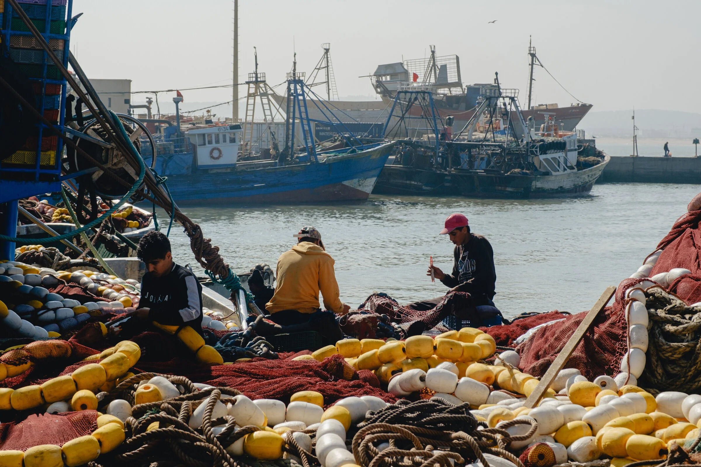 Fishermen mend nets strung with yellow and red floats on the Essaouira docks