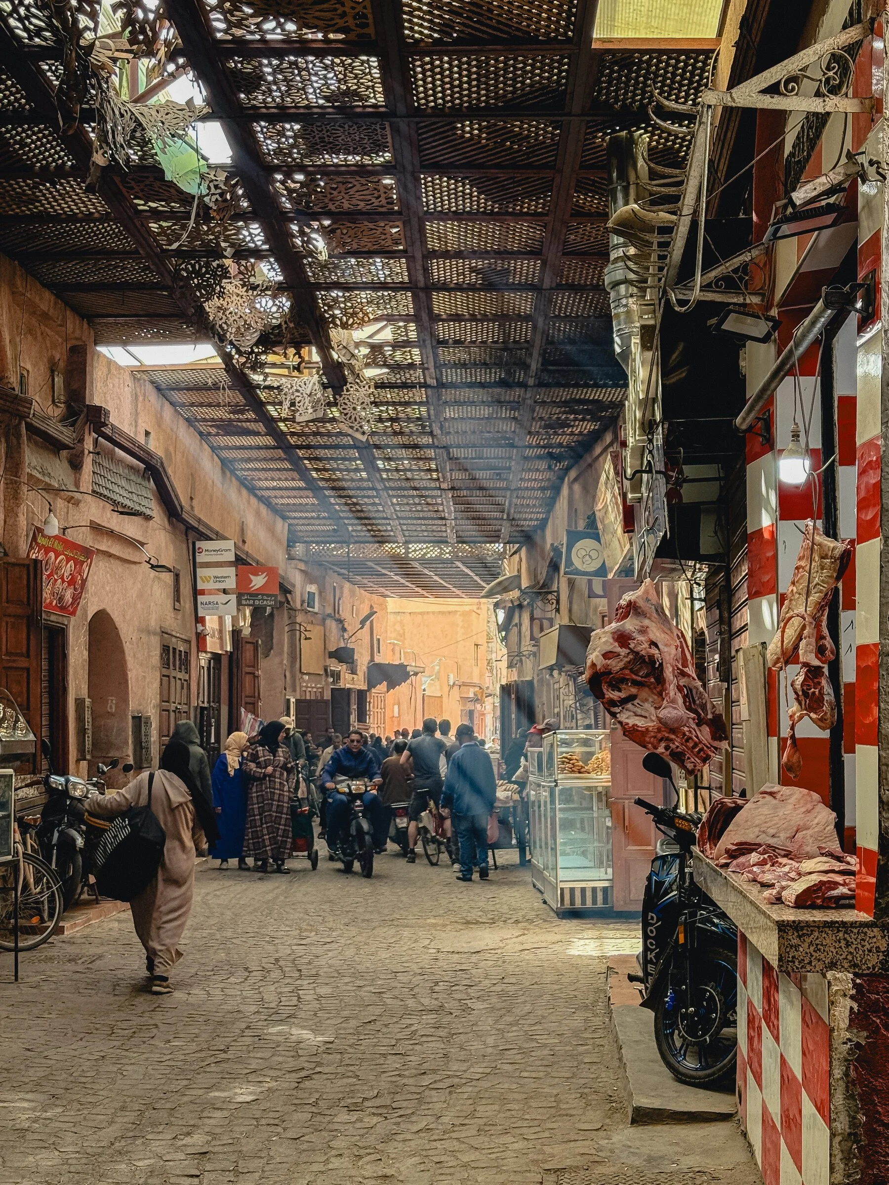 A covered alley in the Marrakech souk, with a butcher stall, motorbikes, and passersby
