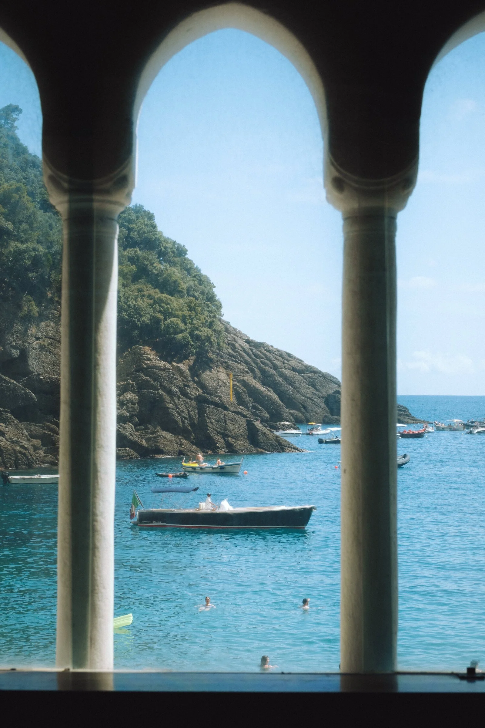 Portofino's harbor and wooded hillside framed through the stone arches of a loggia