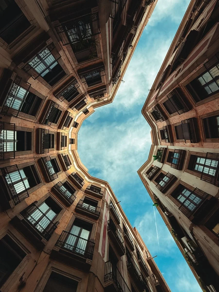 Looking straight up, two apartment buildings converge toward a bright sky