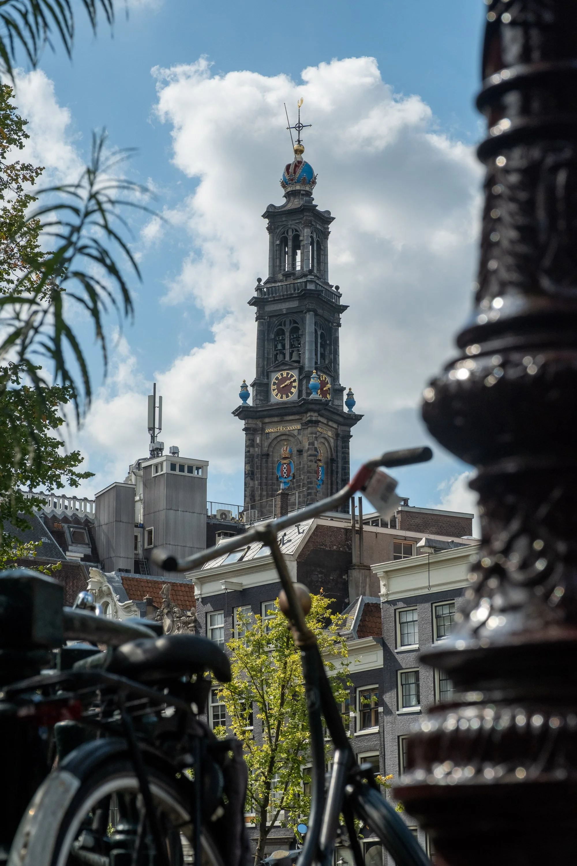 Cityscape with historic clock tower, bicycles parked in foreground, sky with clouds.