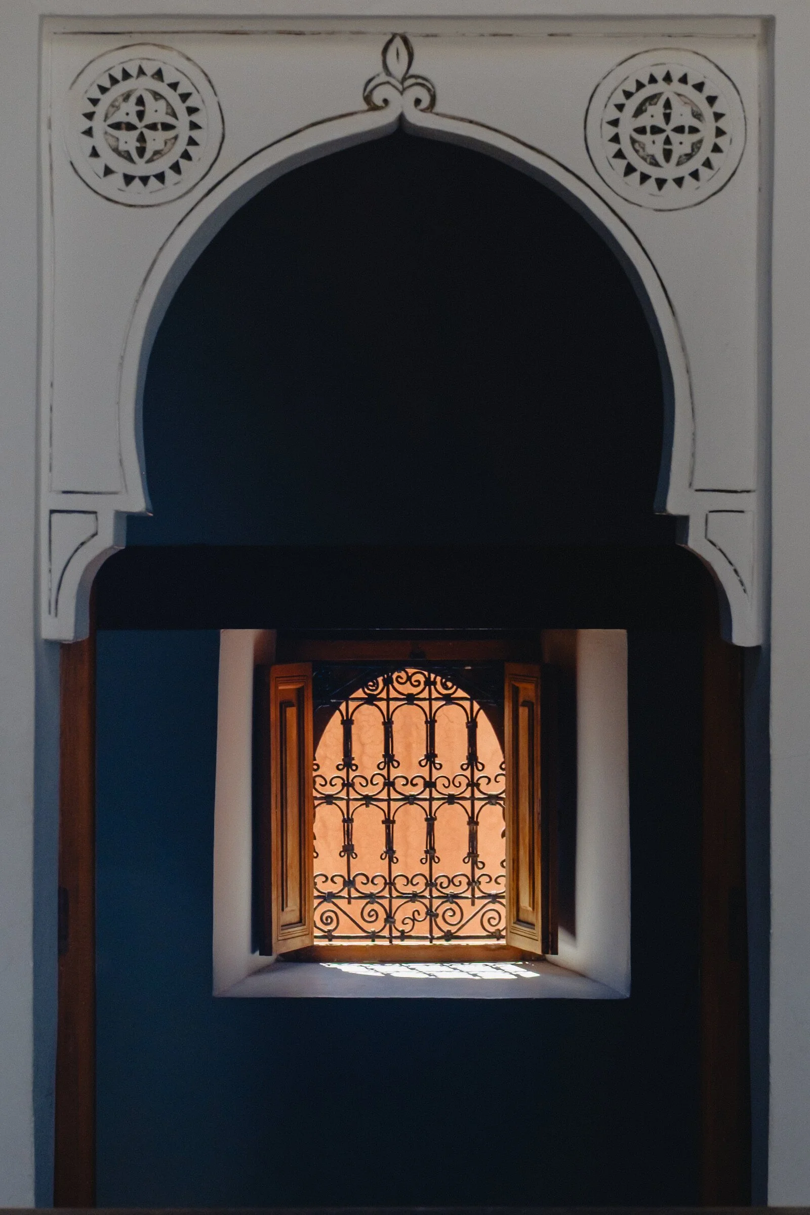 A wrought-iron window glows warm orange within a dark Moorish keyhole archway