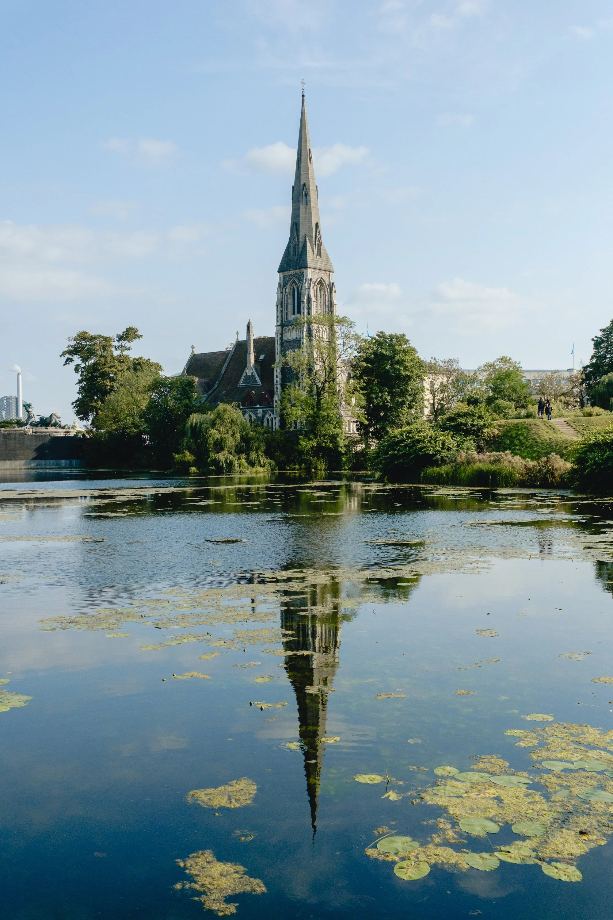 A church with a tall steeple reflected in a lake surrounded by trees.