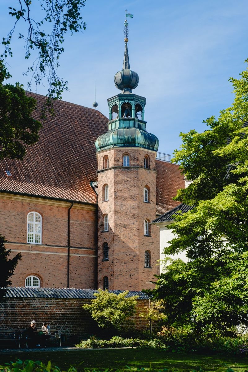 Roskilde Cathedral's brick spire tower crowned with a green copper onion dome, framed by trees