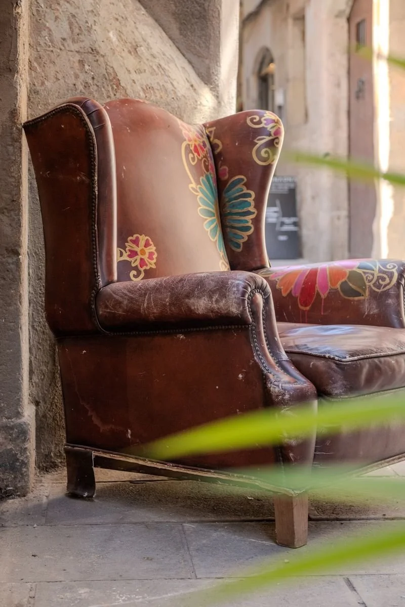 A leather wingback chair hand-painted with colorful flowers sits abandoned on a stone street