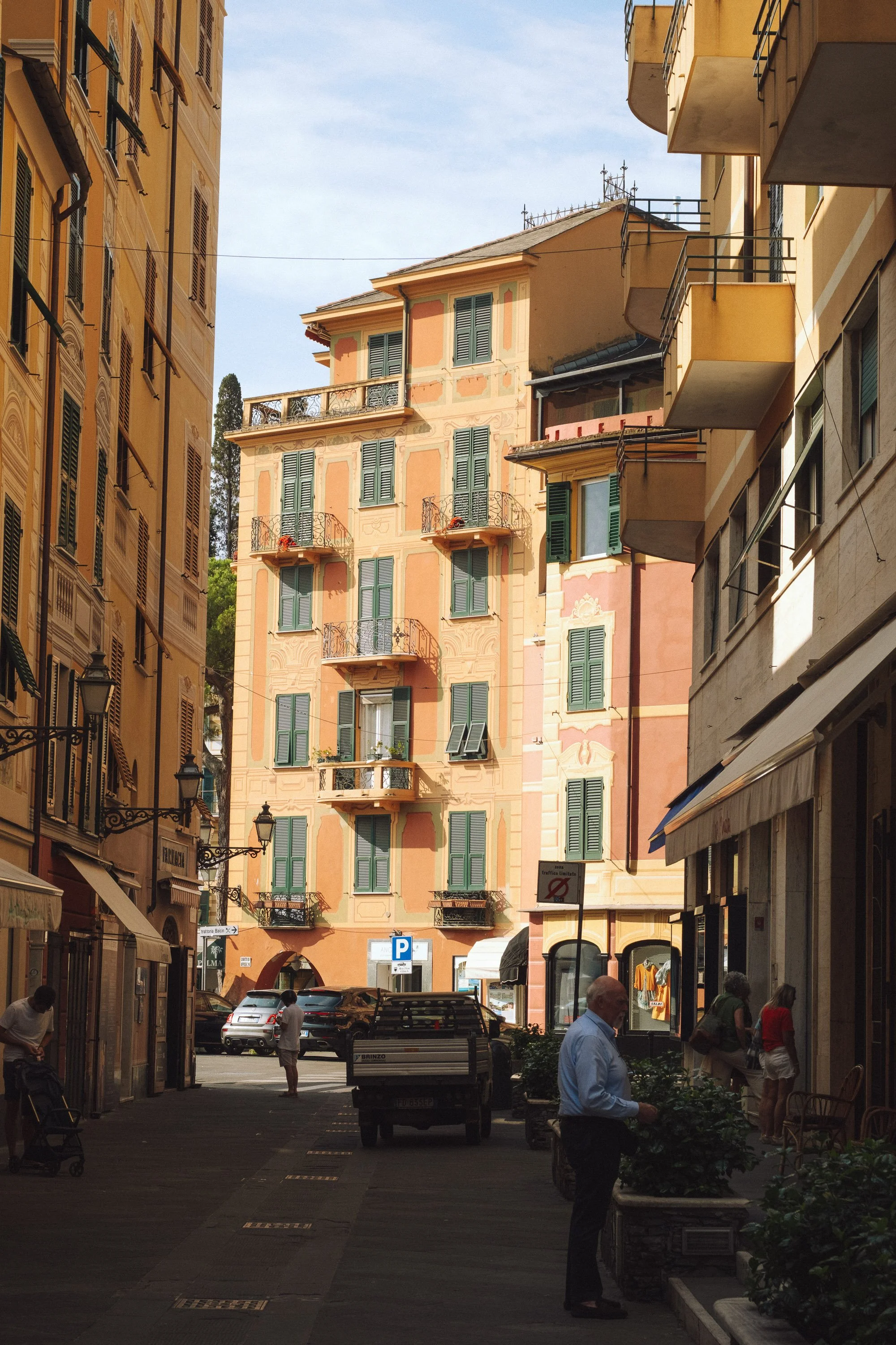 Street view of colorful European buildings with balconies, pedestrians, and parked cars.