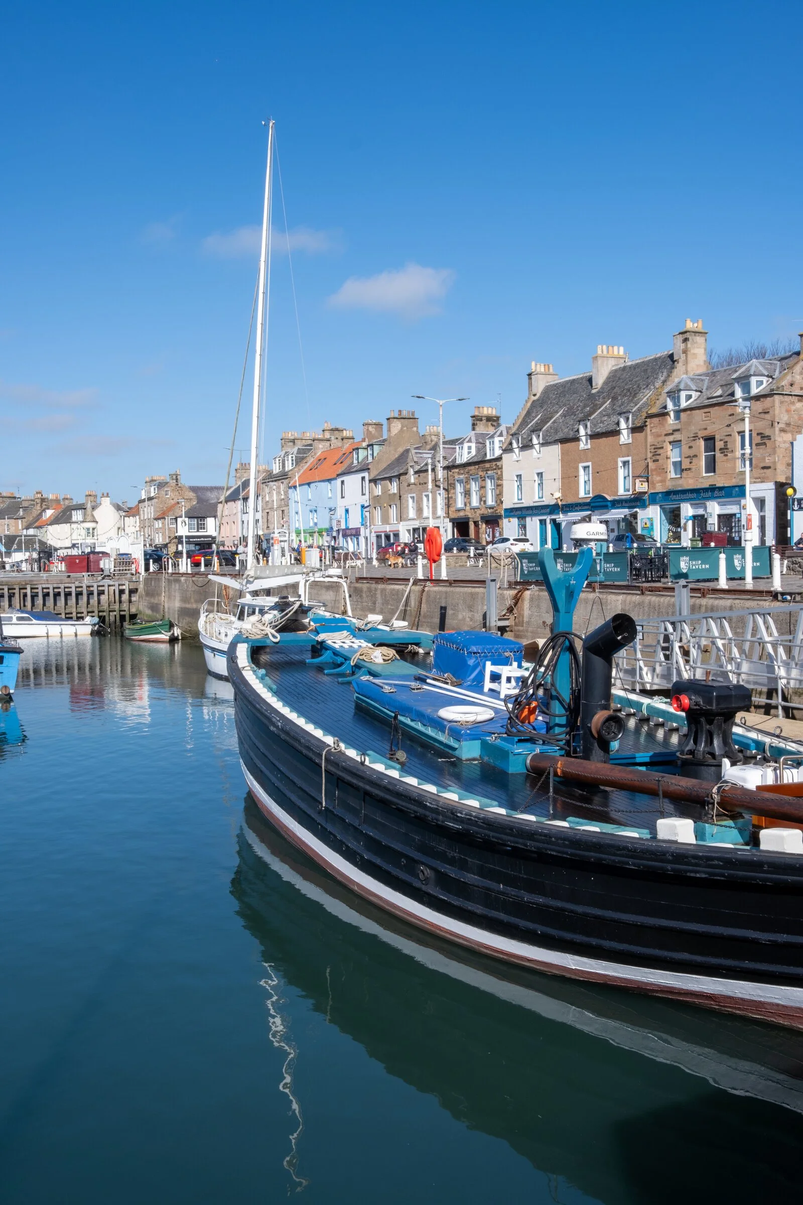 A fishing boat rests at low tide in Anstruther harbor, its reflection still in the water