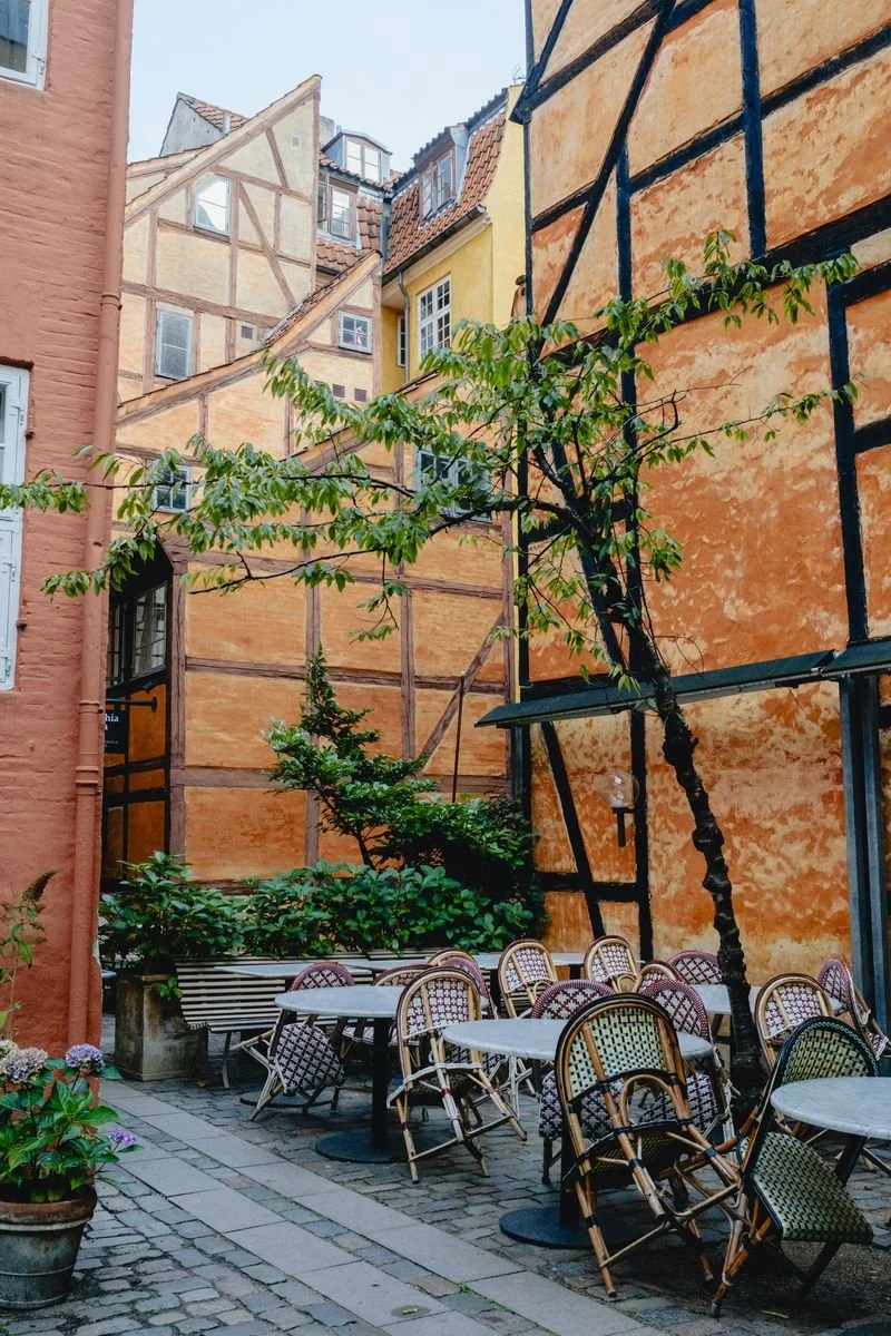 A quiet courtyard cafe with rattan chairs against a weathered orange half-timbered building
