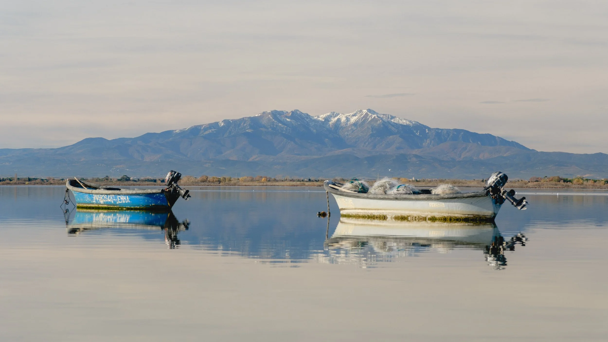 Two small boats floating on calm water with snow-capped mountains in the distance.