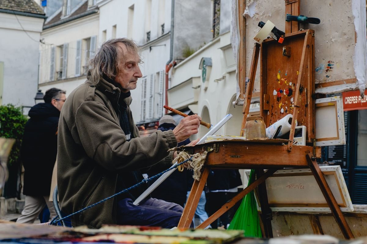 A street painter concentrates on his canvas at an easel on a Montmartre street