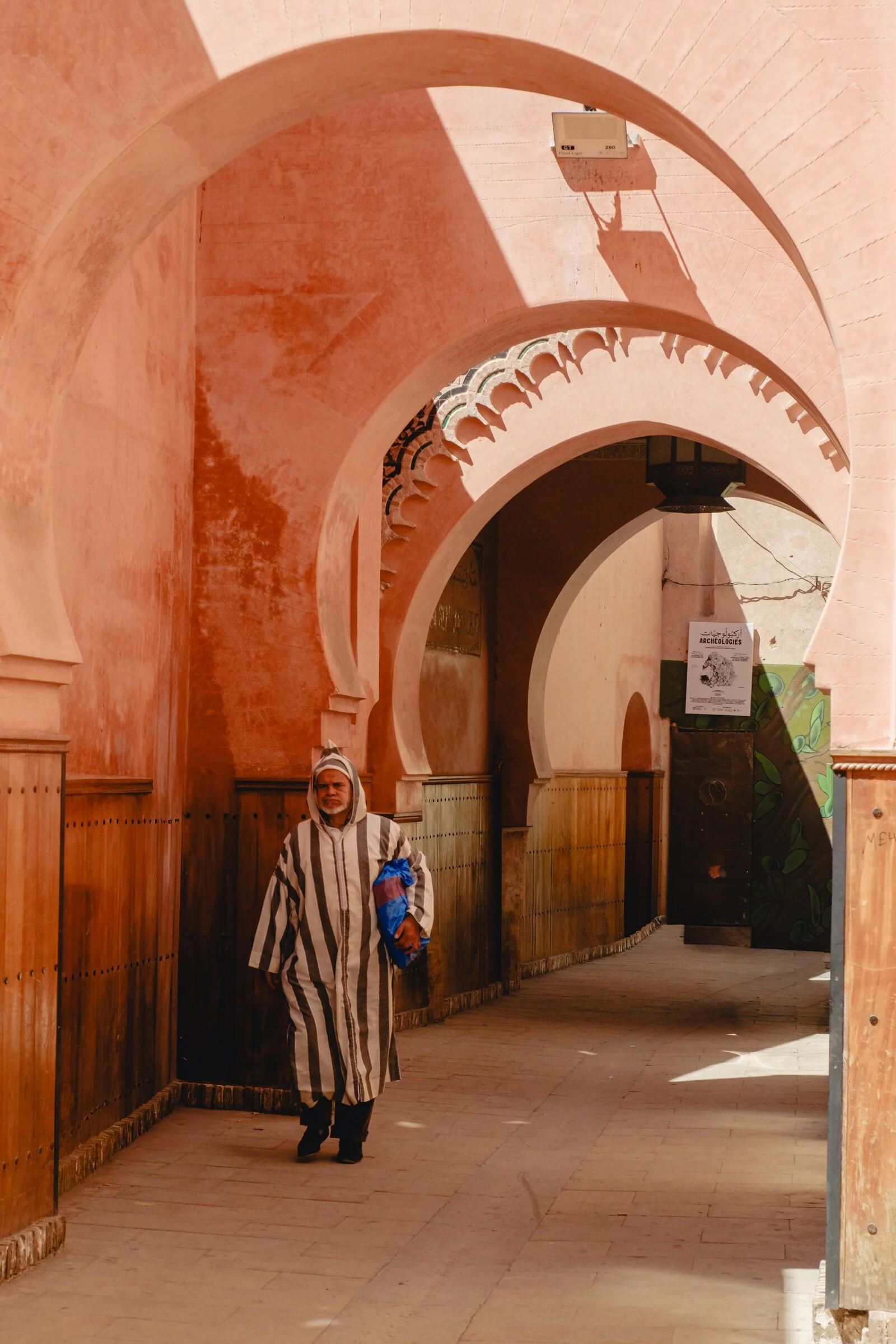 A man in a striped djellaba walks beneath Marrakech's pink arched arcades