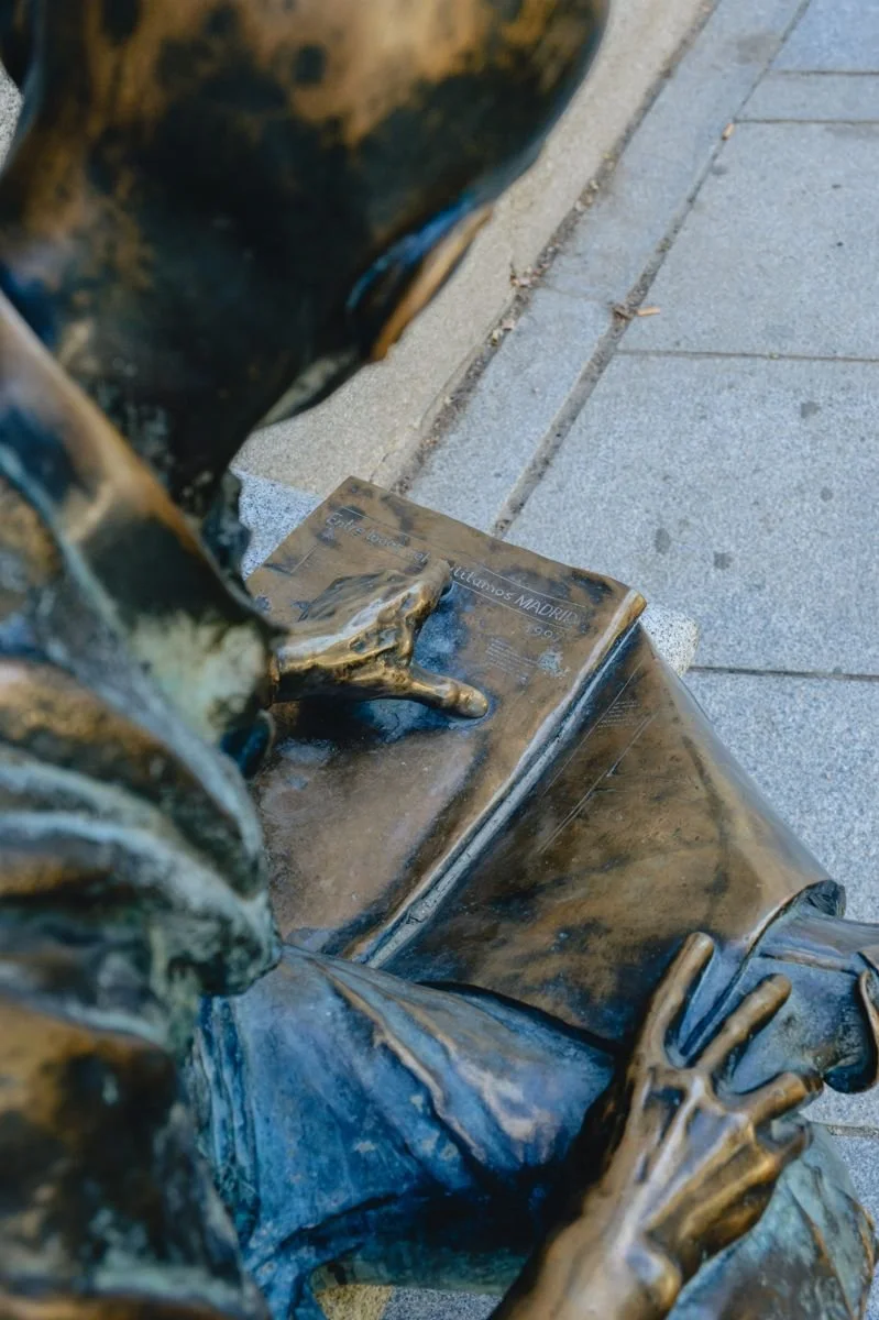 Close detail of a bronze street sculpture, a hand resting on an open book