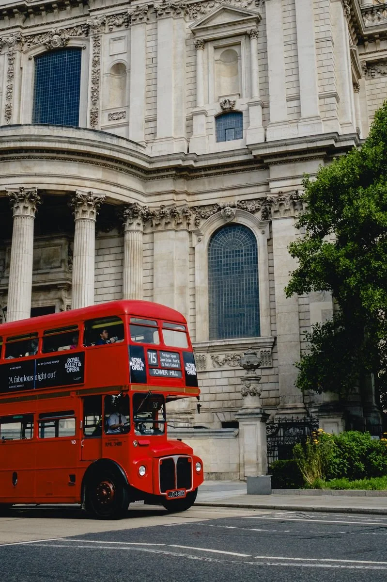 A red double-decker bus passes beneath St Paul's Cathedral's colonnade