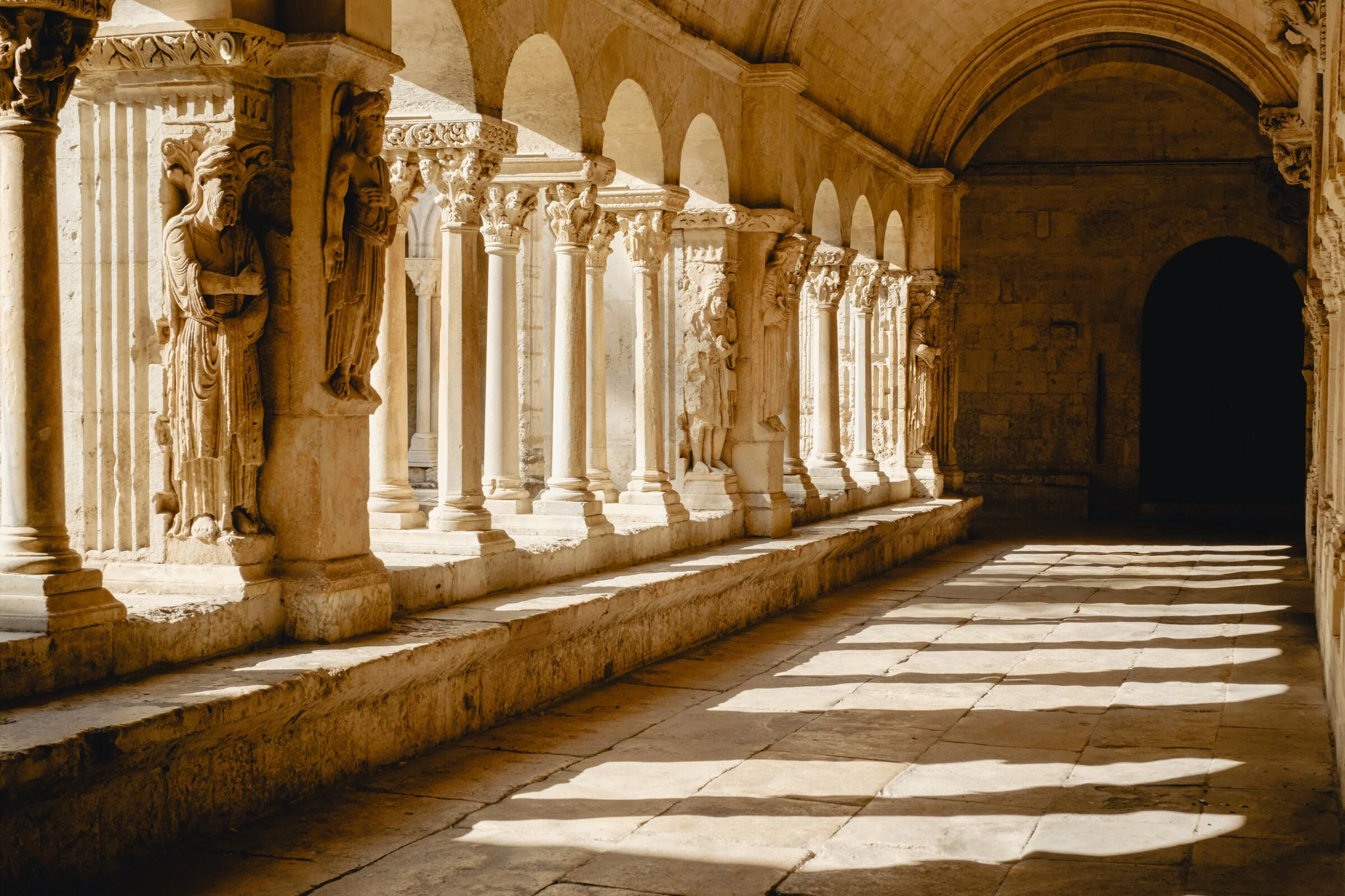Weathered stone figures of apostles stand among carved columns in the Romanesque cloister gallery of Saint-Trophime, Arles
