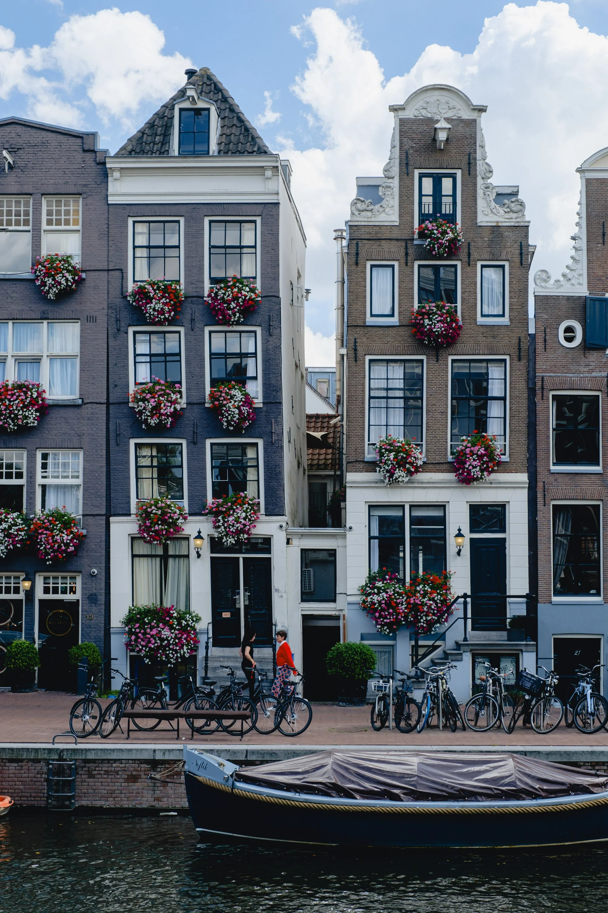 Fine art photograph of Amsterdam canal houses in bloom. A romantic European city print with flowers, bicycles, and soft summer light.