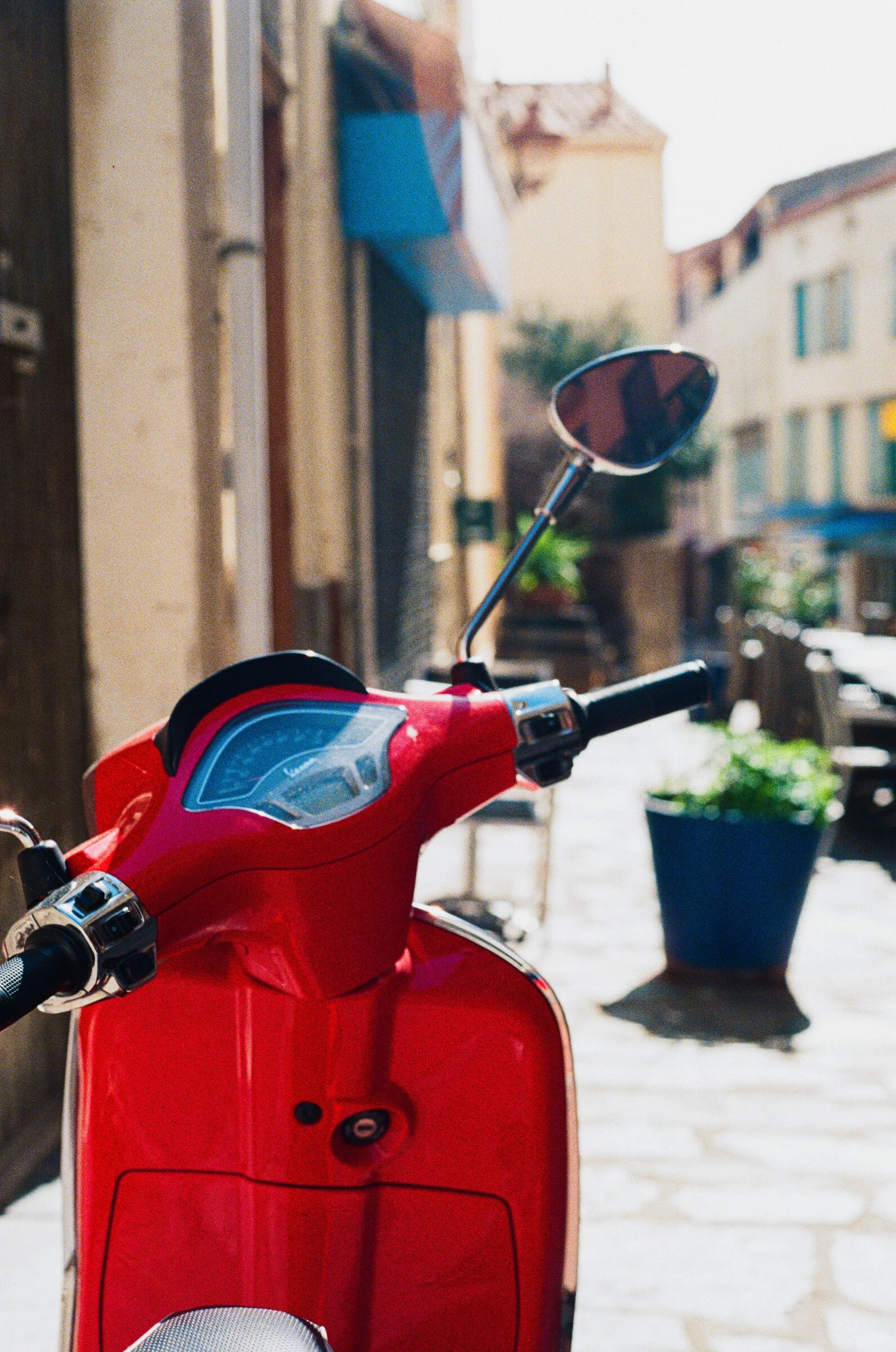 A cherry-red vespa scooter parked in a narrow sunlit alley in Collioure